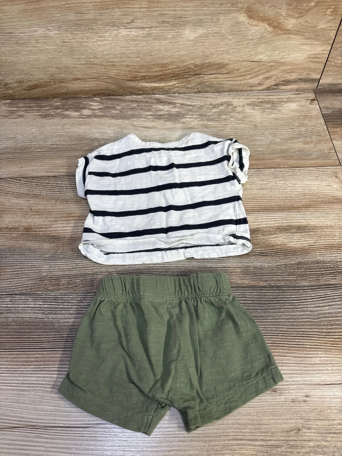 Top-down view of newborn striped henley shirt and shorts set showcasing navy horizontal stripes and olive elastic-waist shorts on wood floor