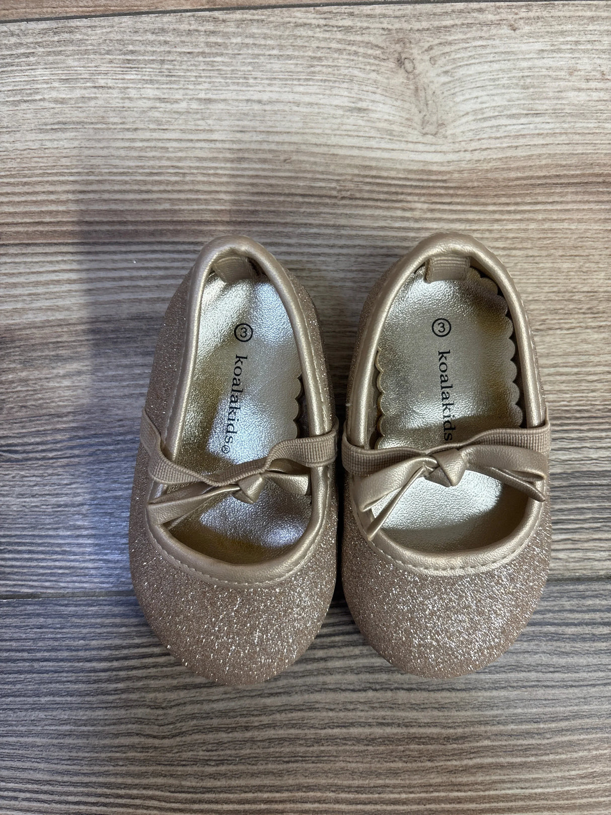 Top view of Koala Kids glitter bow ballet flats size 3C showing gold glitter finish, bow strap and metallic insole on wood