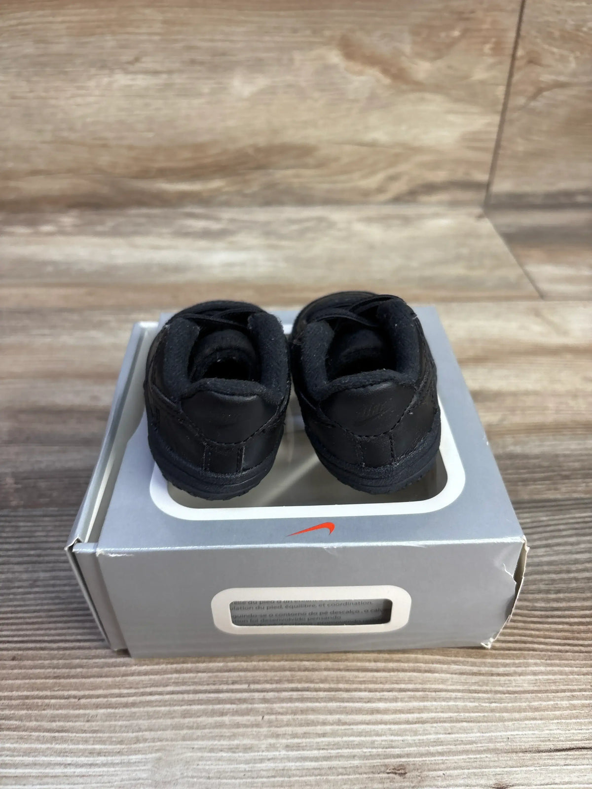 Rear view of Nike Air Force 1 crib shoes in black, size 1C, showcasing padded collars on a gray shoebox