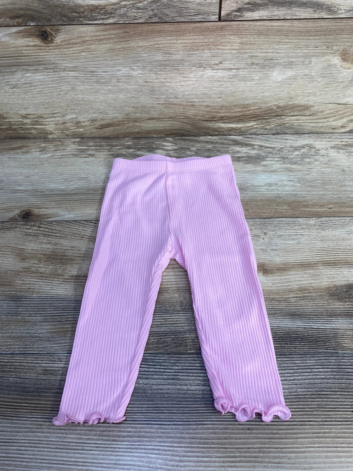 Flat lay of pink ribbed toddler leggings showing ruffled hem and elastic waistband on light wood background