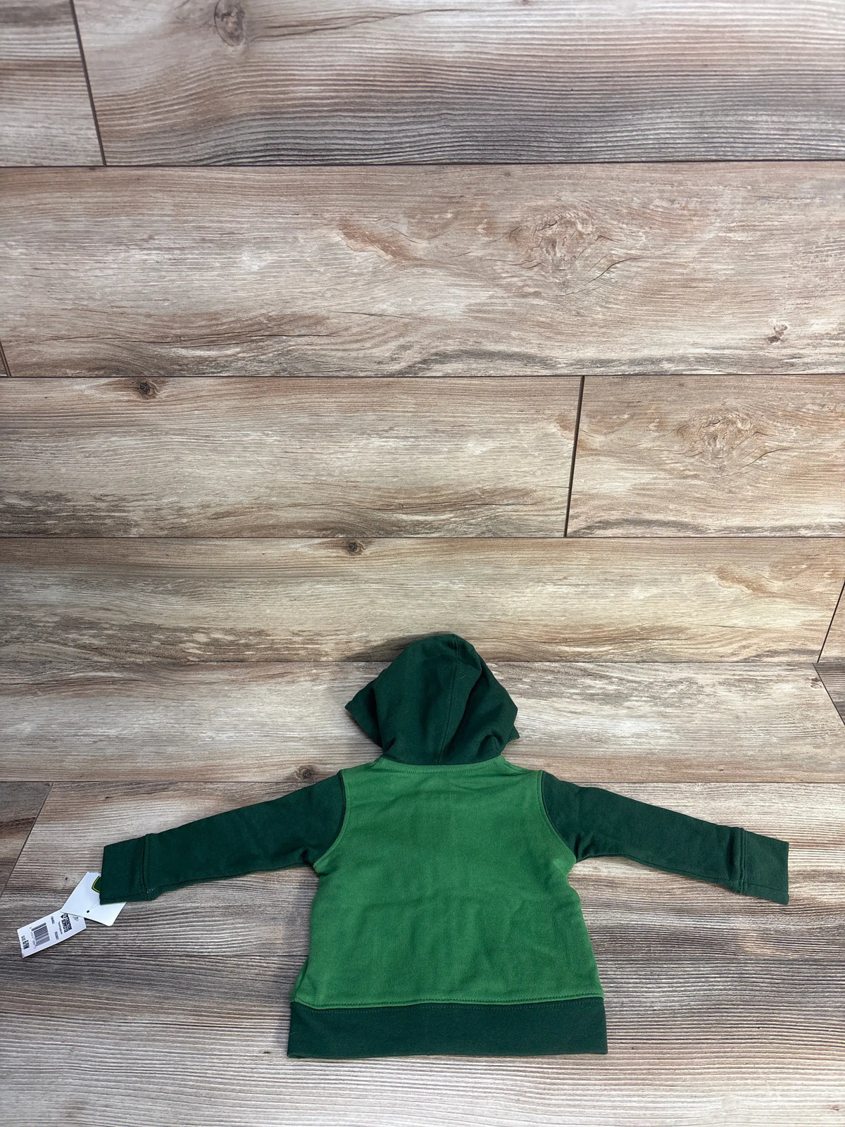 Back view of a green John Deere full-zip hoodie for size 6/9 months showcasing its hood and long sleeves on a wood-look floor