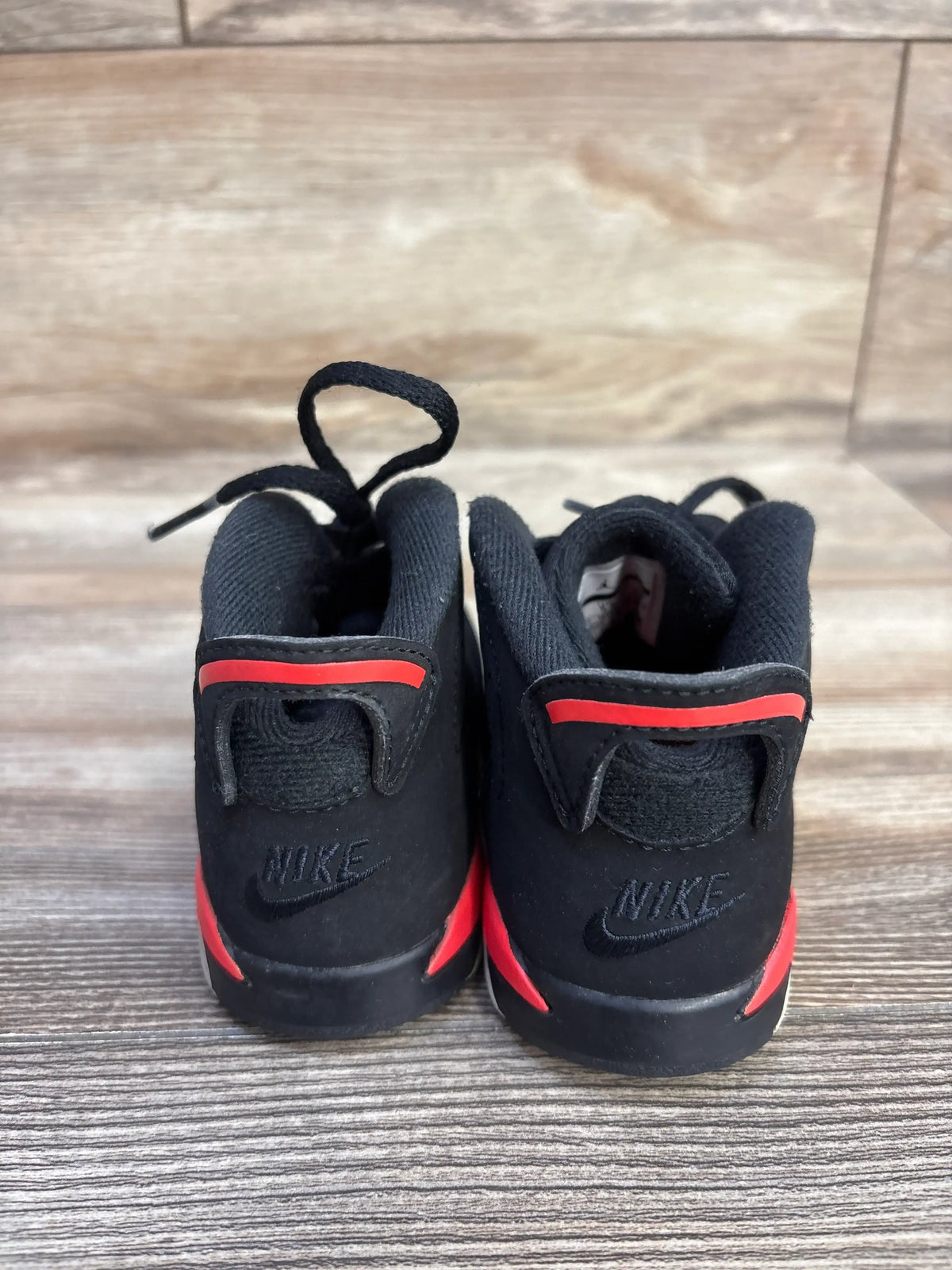 Rear view of Air Jordan 6 Retro TD Infrared sneakers showcasing black uppers, red accents, and heel branding on a wood floor