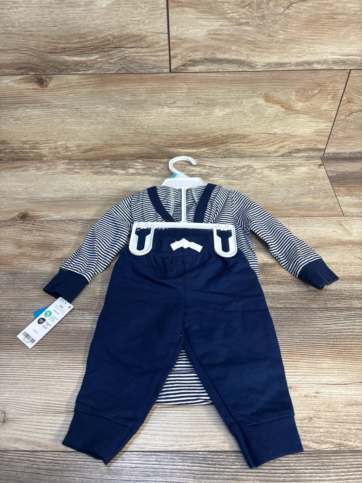 Striped long sleeve baby romper with navy overalls and bow detail on wood floor