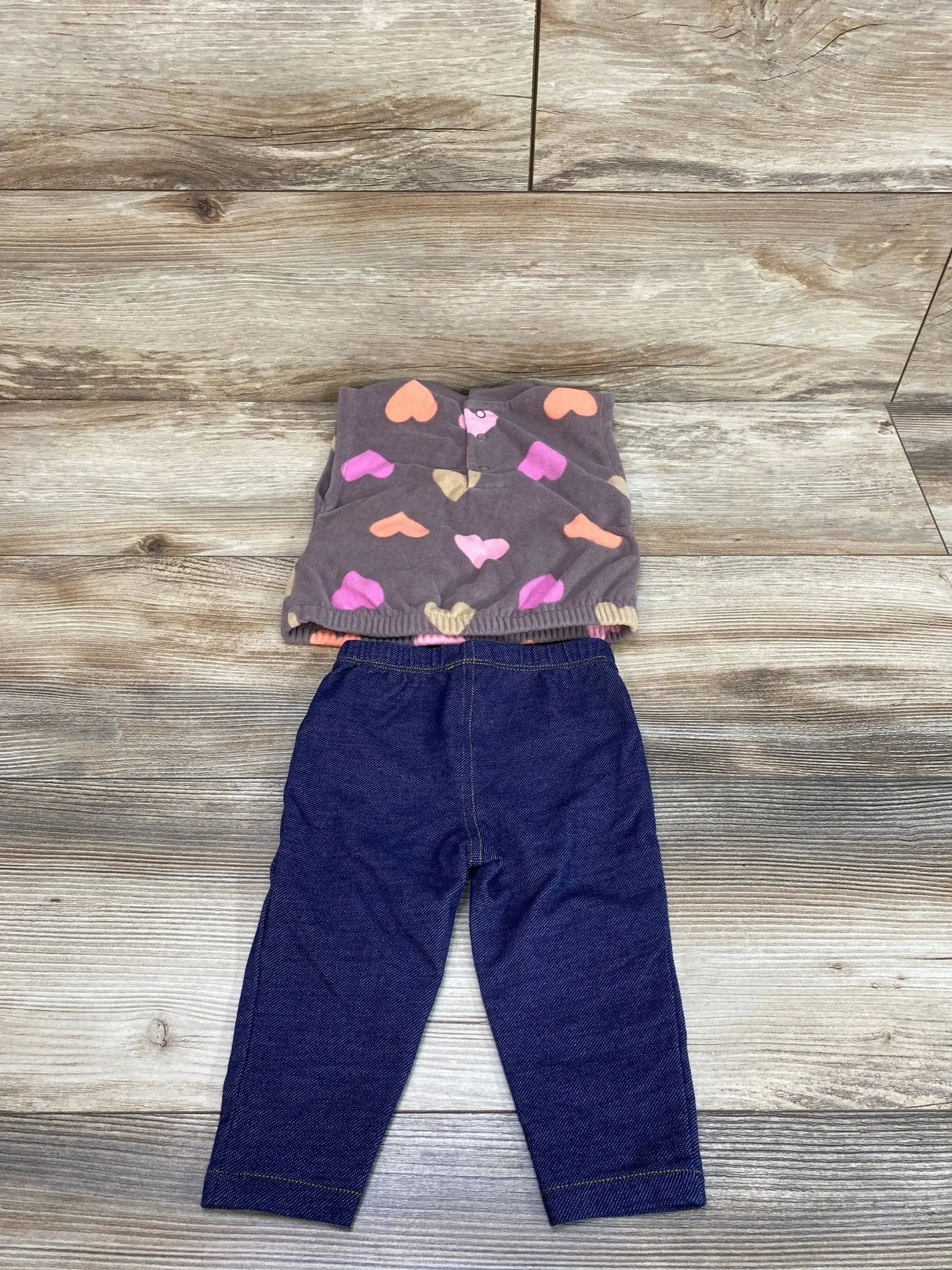 Flat-lay of Carter's 2-piece set: brown fleece vest with multicolored hearts and navy leggings, size 6 months, showing elastic waistband on wood background