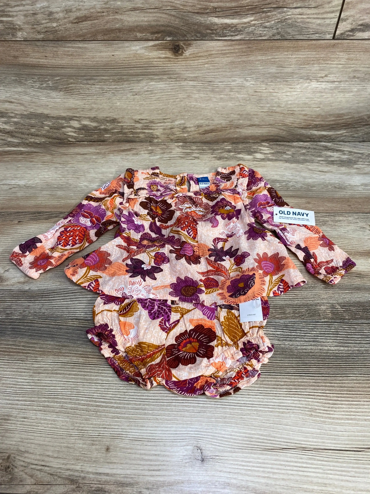 Flat lay of Old Navy pink floral baby top and matching bloomers with ruffled neckline and ruched legs on wood background
