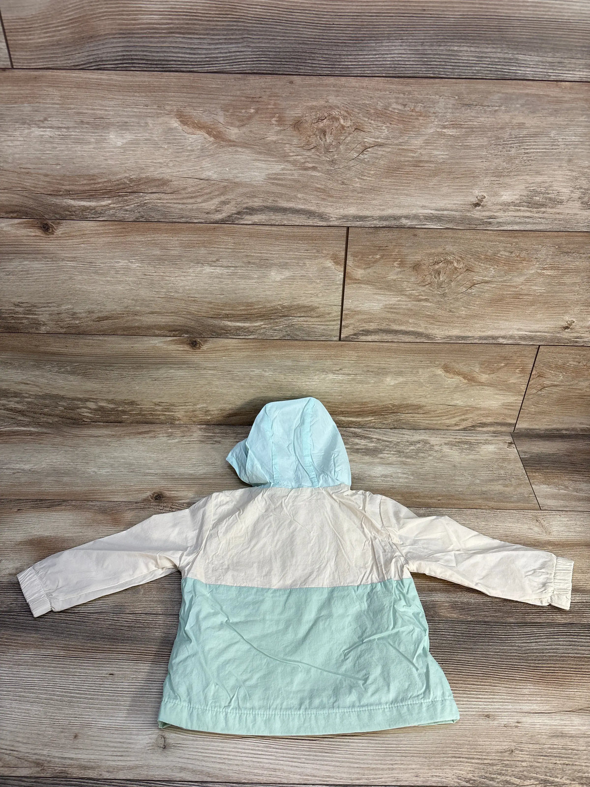 Back view of Cat & Jack colorblock hooded windbreaker in cream and aqua, size 18m, on a wood background