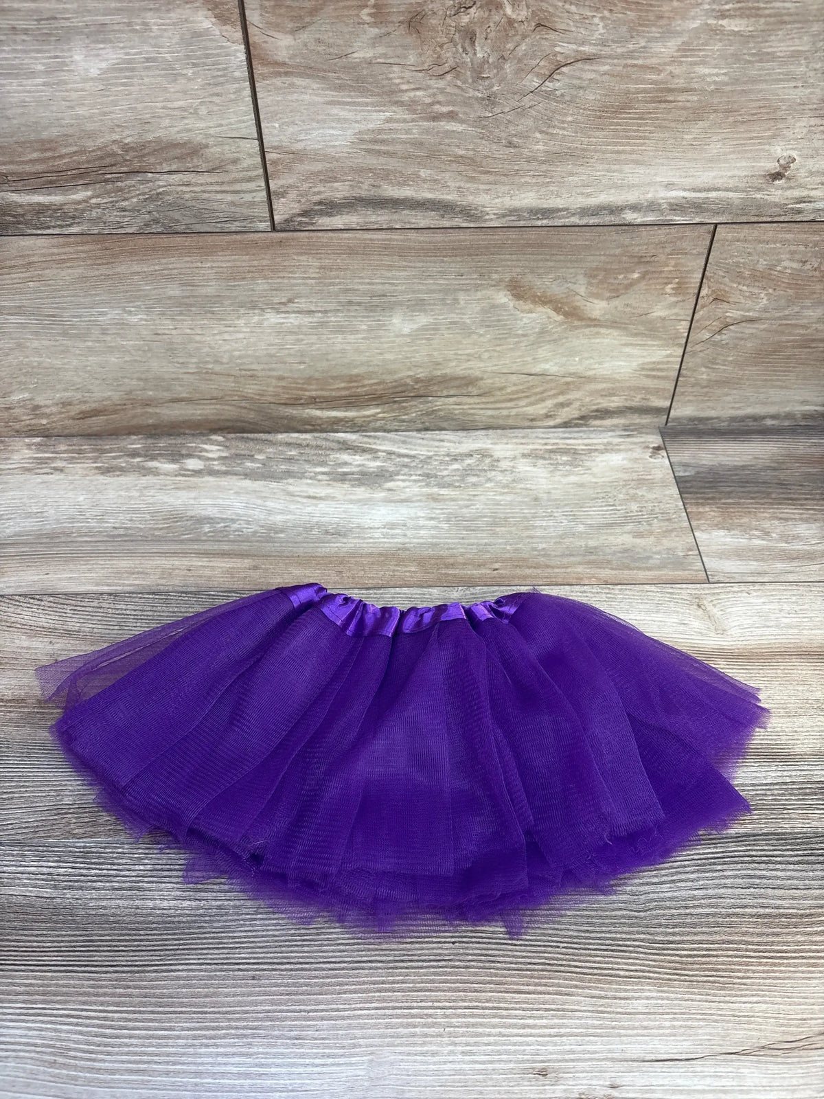 Flat lay of purple toddler tutu skirt (6-18 months) showing layered tulle and satin elastic waistband on light wood background