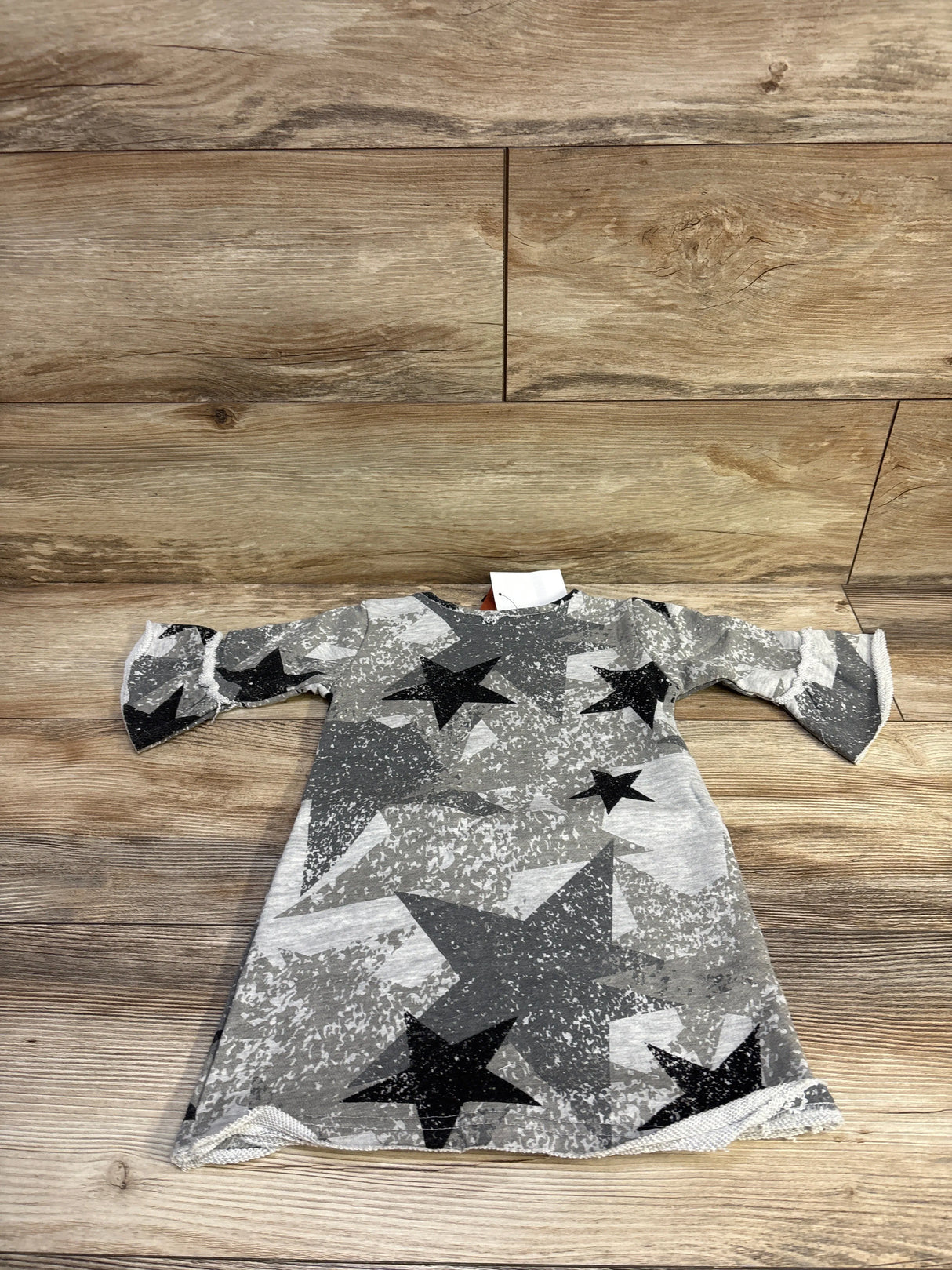 Flat lay of Appaman Kathleen toddler dress showing grey camo star print and three quarter bell sleeves on wood background