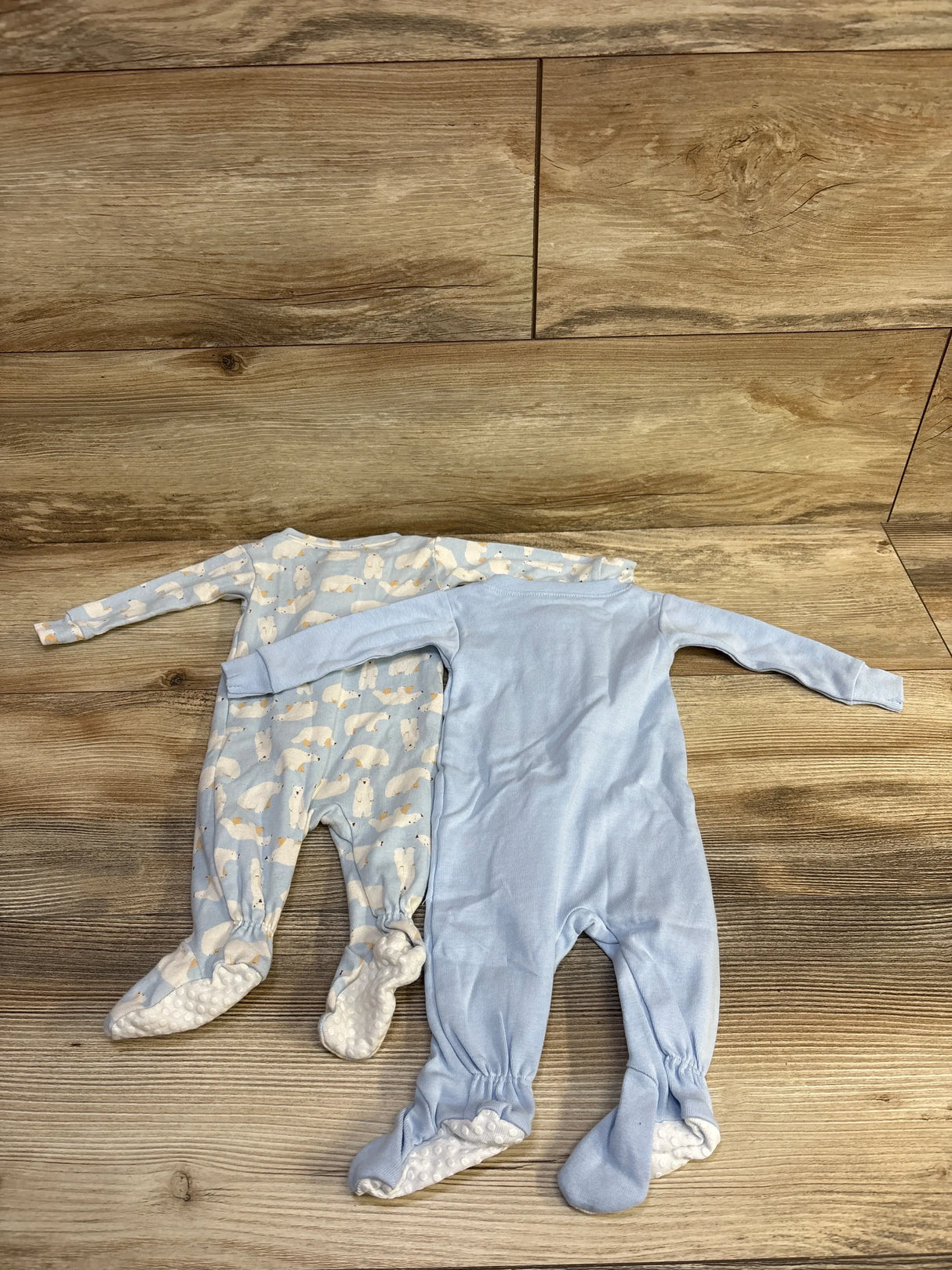 Top-down view of two newborn light blue footed sleepers showcasing one polar bear print and one solid design with wooden floor background