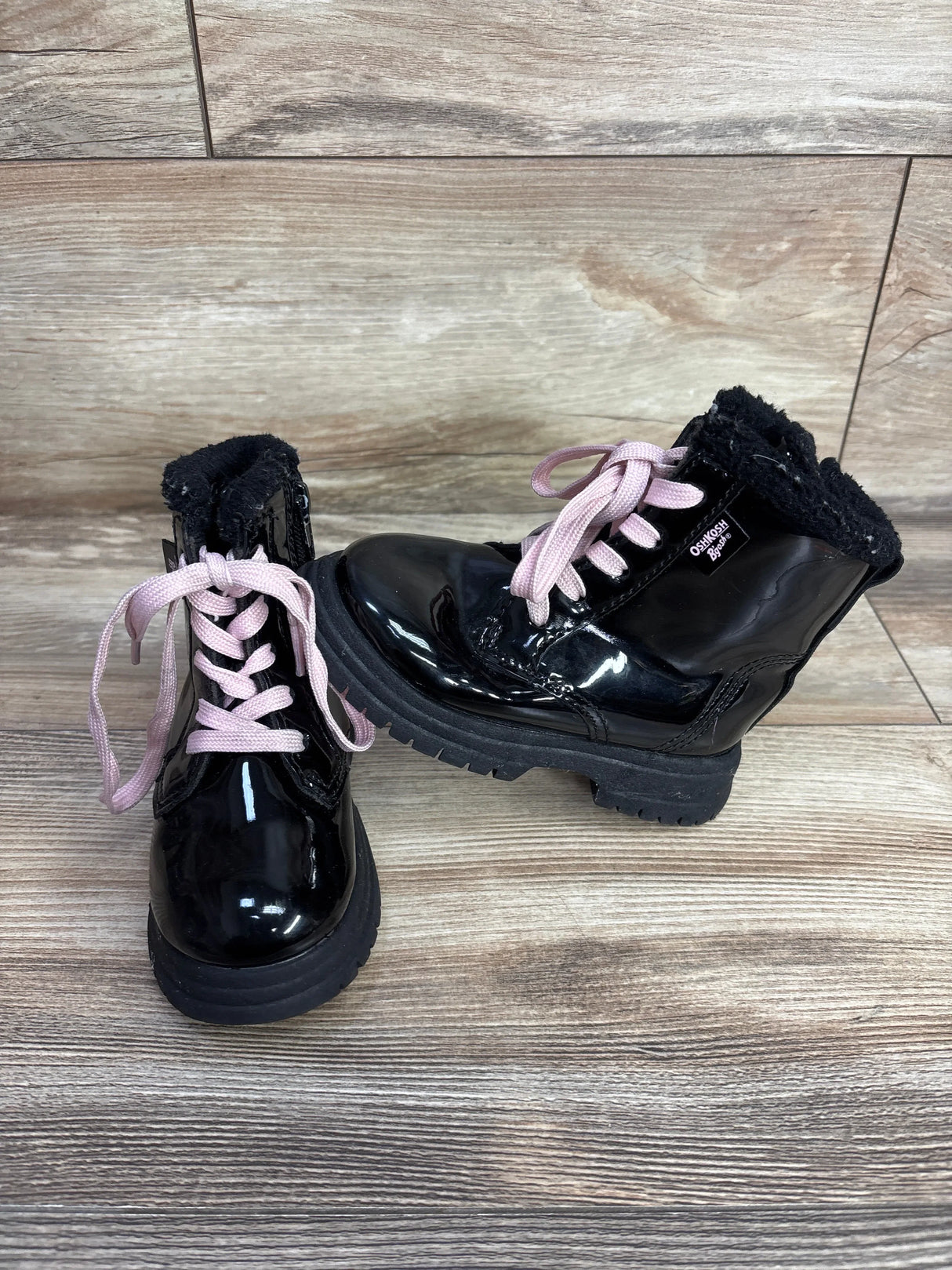 Glossy black OshKosh B'gosh toddler boots with pink laces and black fur lining on wood backdrop