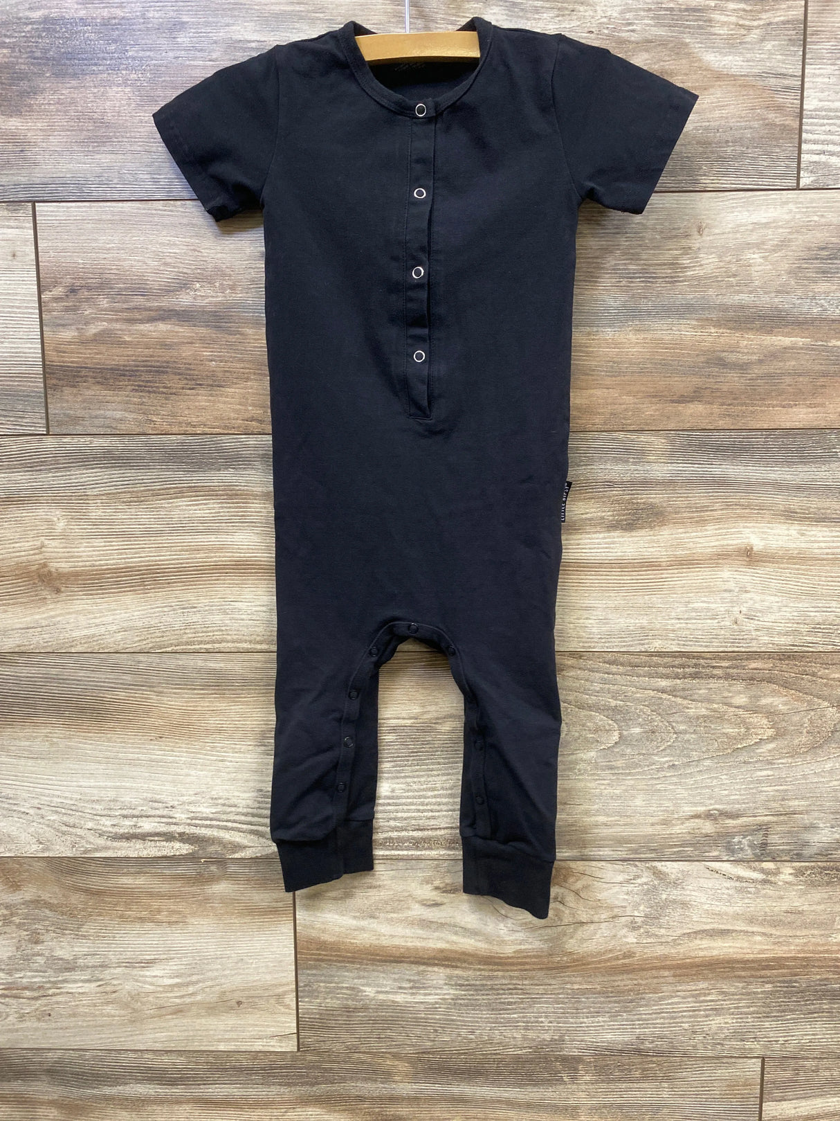 Black short-sleeve baby romper with snap buttons on front and legs on wooden floor background