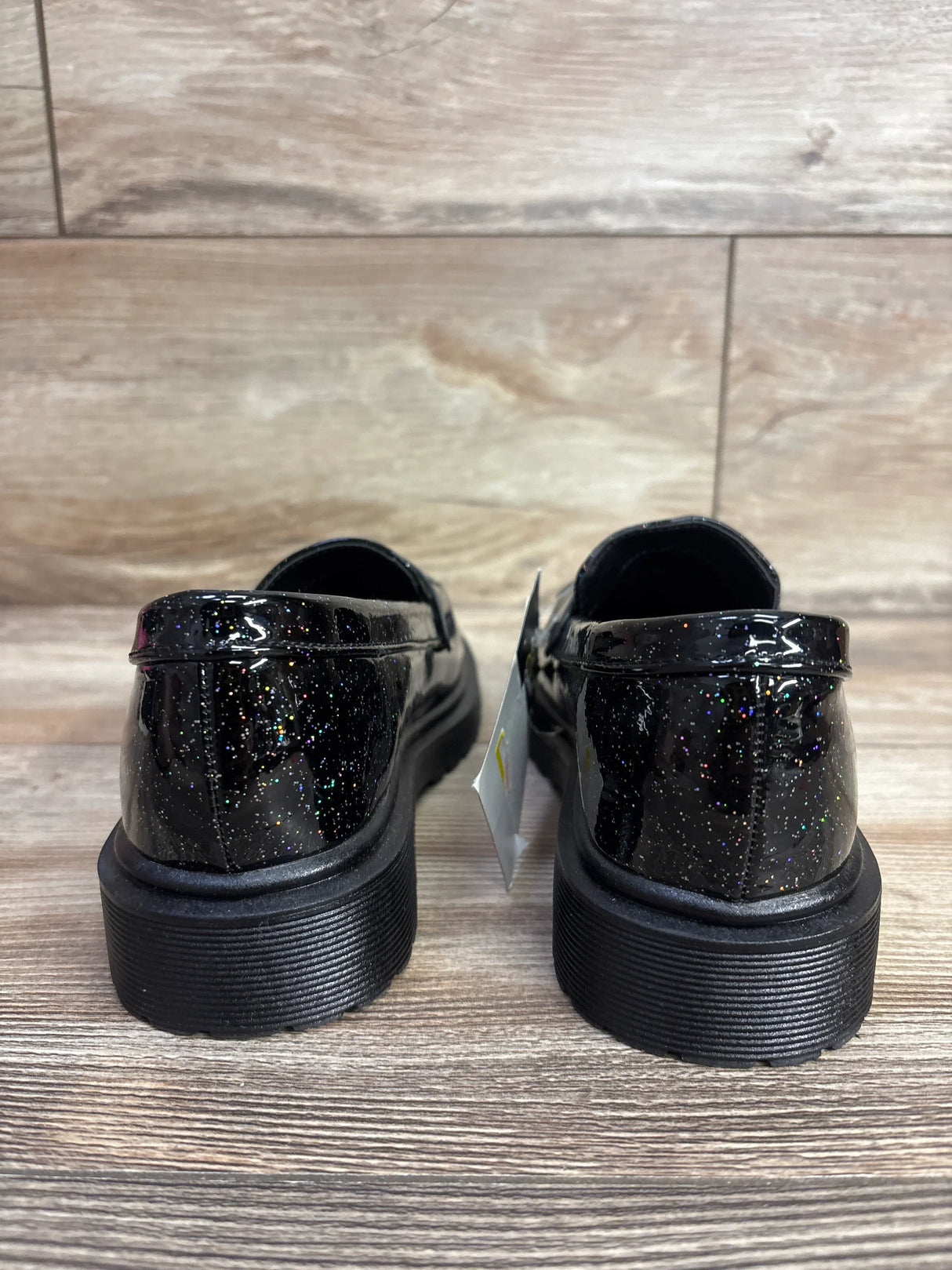 Rear view of black glittery kids patent leather dress shoes on wood floor