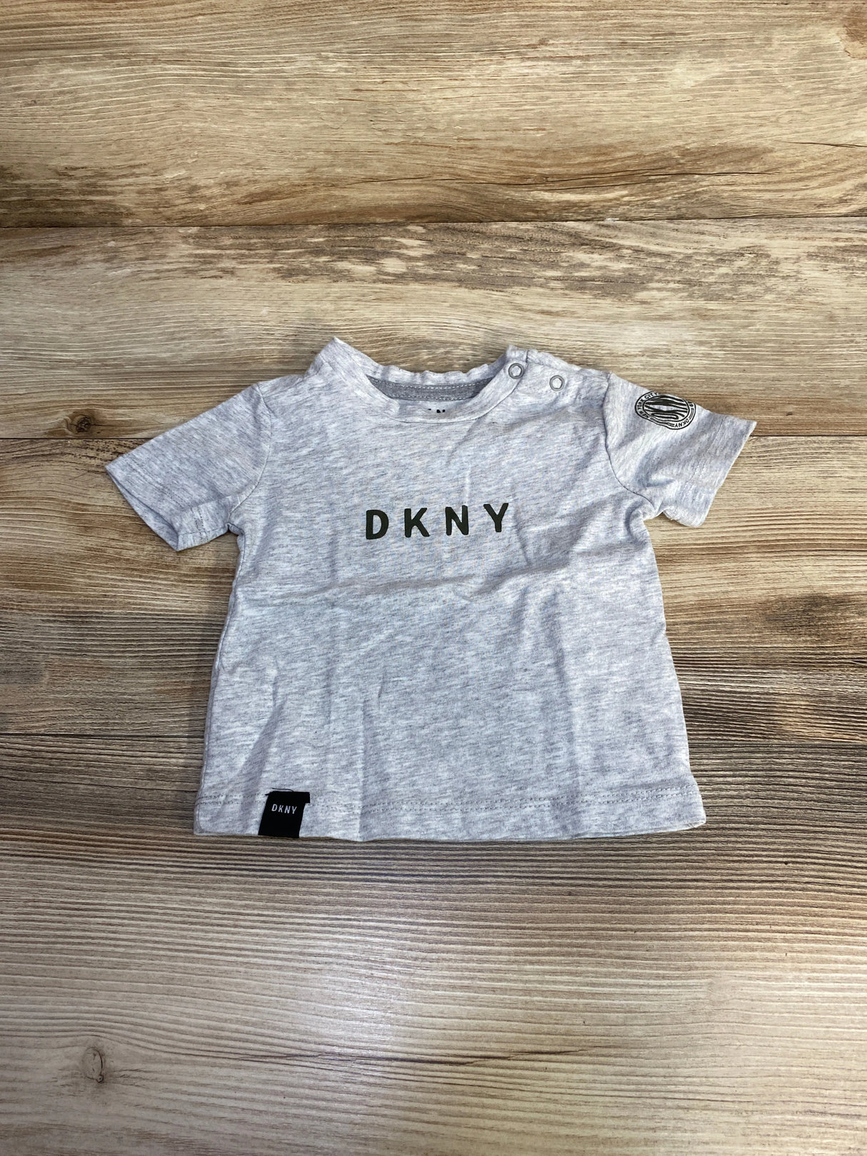 Light grey DKNY baby t-shirt on wood background, short sleeves, logo on chest and sleeve