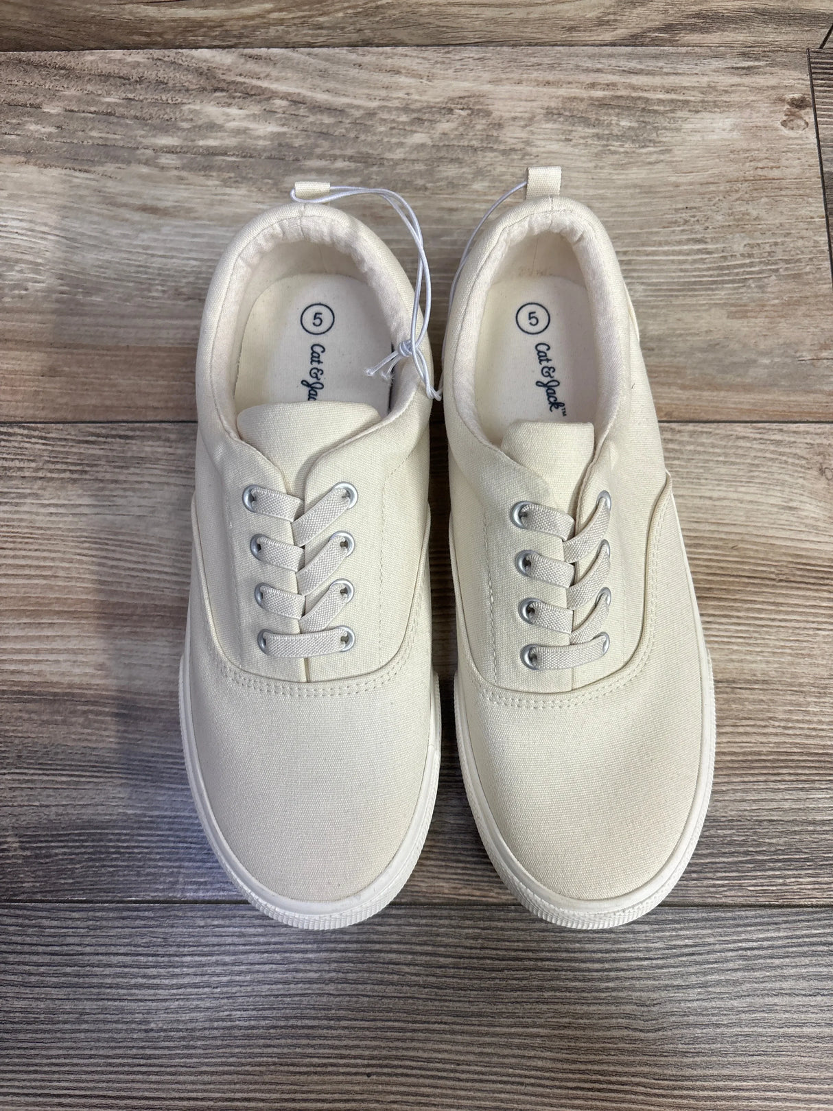 Pair of white Cat & Jack kids' sneakers size 5 on wooden floor background at kids resale store
