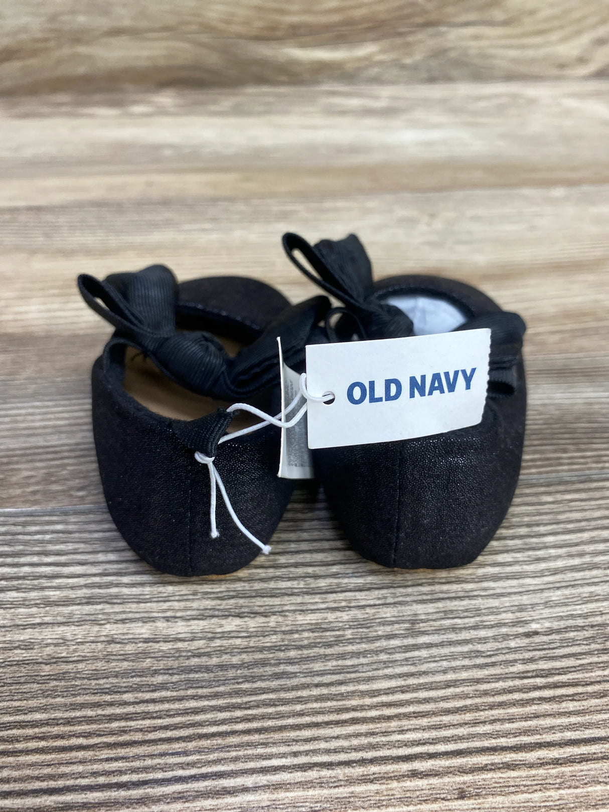 Pair of black Old Navy baby ballet flats with bows on a wooden surface