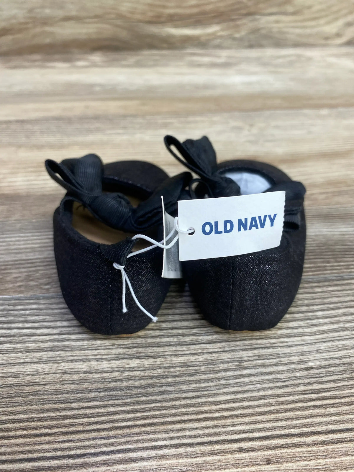 Front view of Old Navy canvas baby ballet flats showcasing black grosgrain bows and attached Old Navy tag on wooden surface