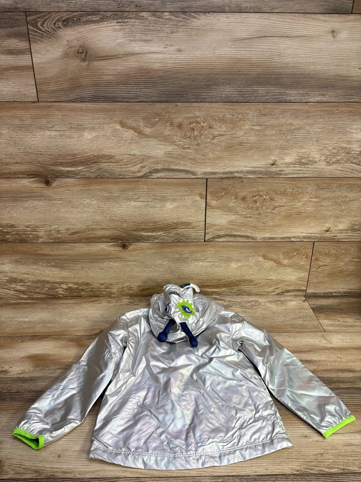 Flat lay of new Cat and Jack holographic rain jacket size 5T in silver grey with hood neon green cuffs and navy drawstring on wood plank floor