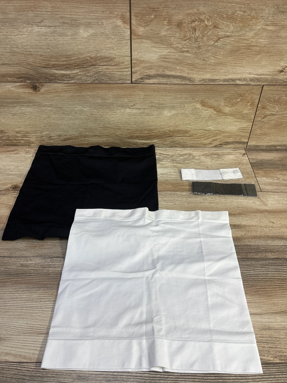 Flat lay of Kunindome maternity 4-piece waist extenders and belly bands showing black and white bands and two packaged extenders on wood background