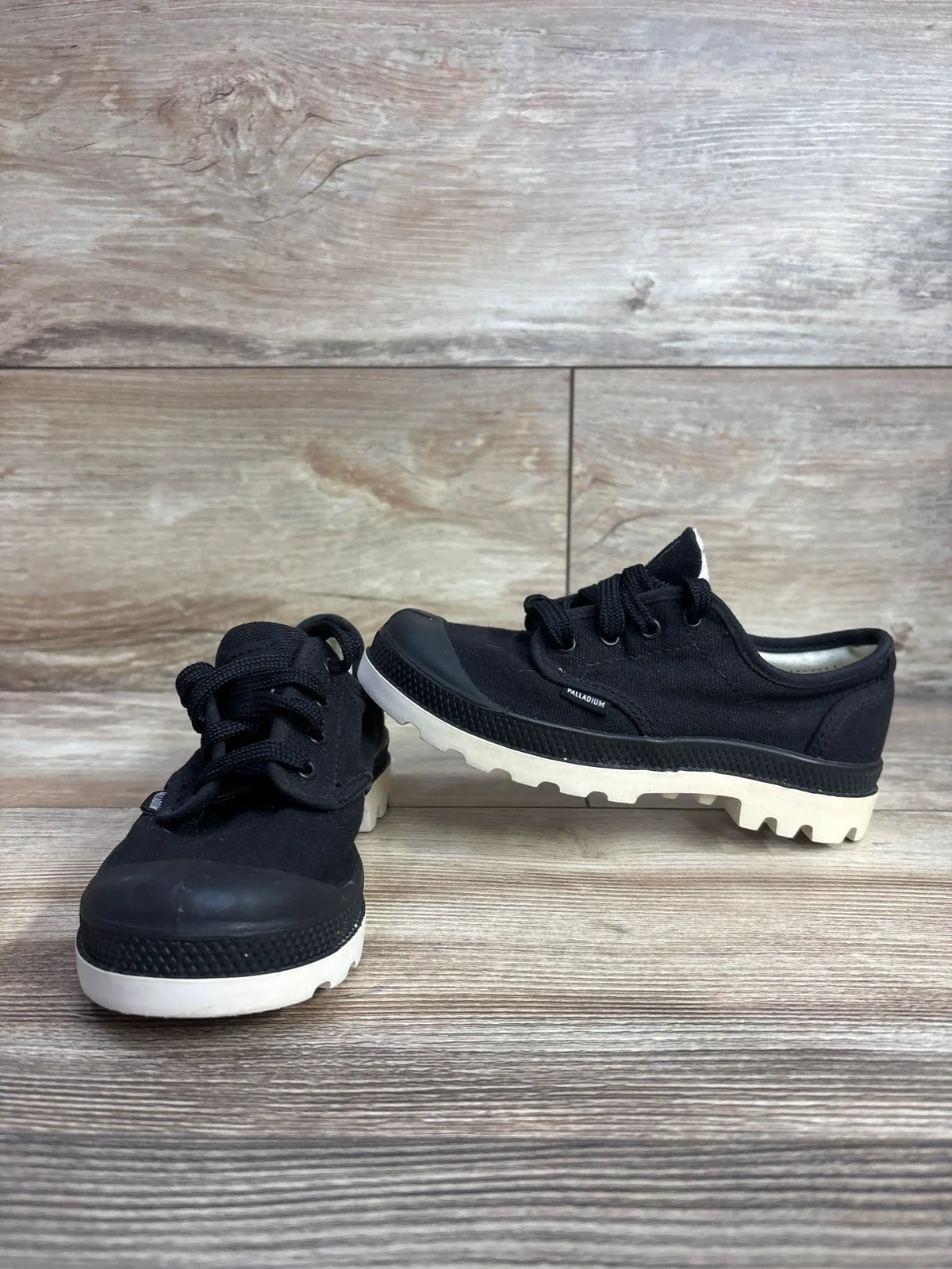 Pair of black Palladium kids canvas sneakers with white rugged soles on wooden floor