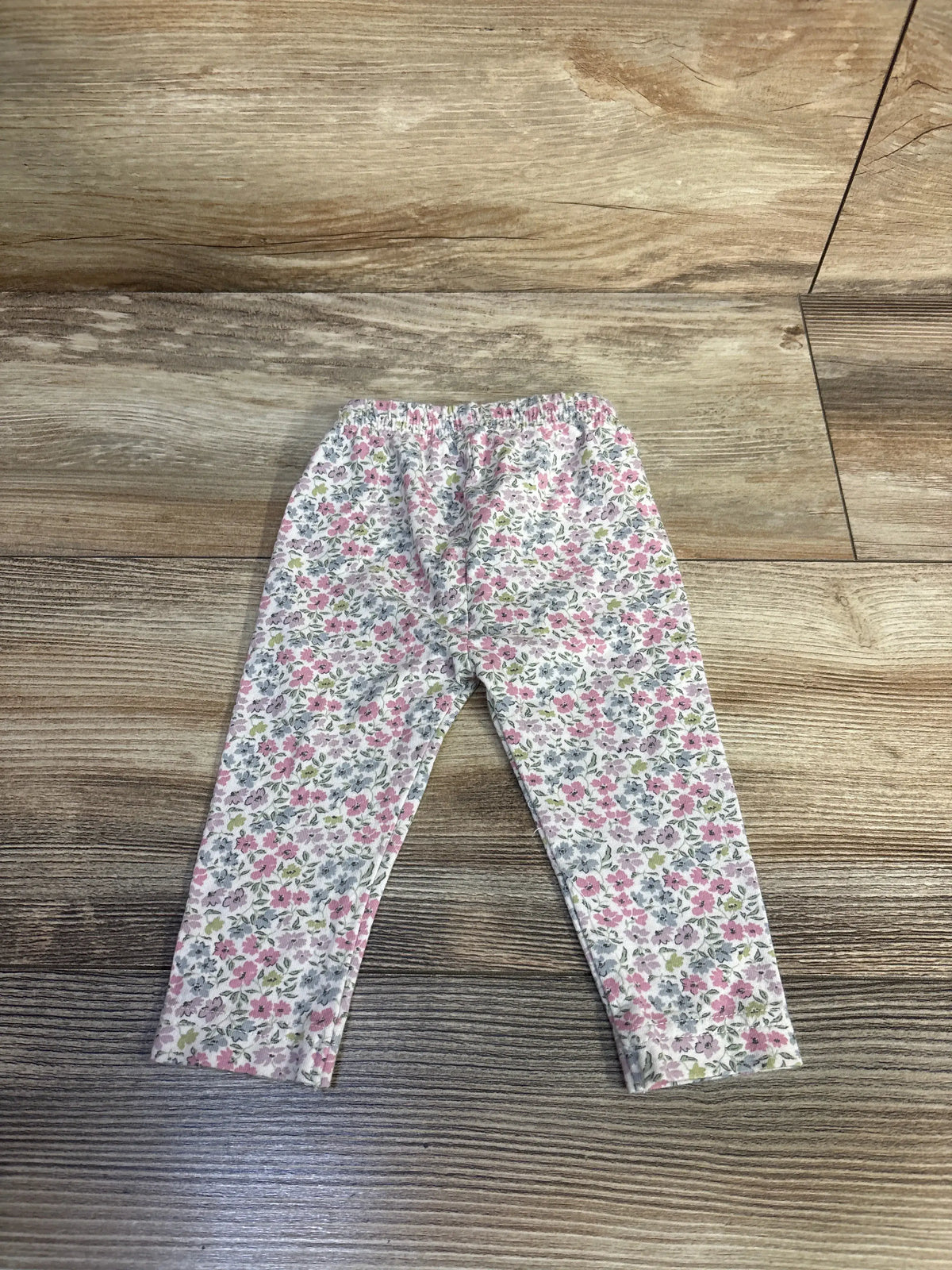 Flat lay of Jamie Kay newborn floral leggings showcasing a pink and gray floral print on white fabric with a wood floor