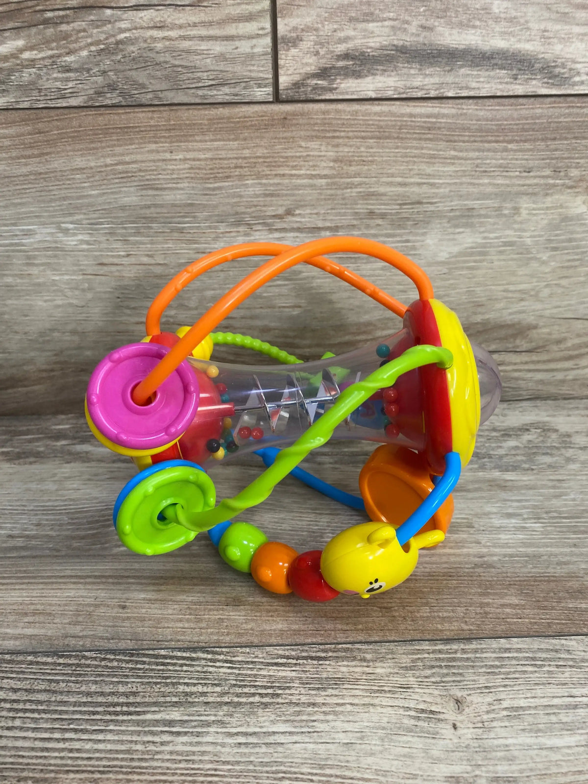 Angled view of Grab N Shake sensory ball with clear rattle, multicolored beads, and wire bead loops on wood surface