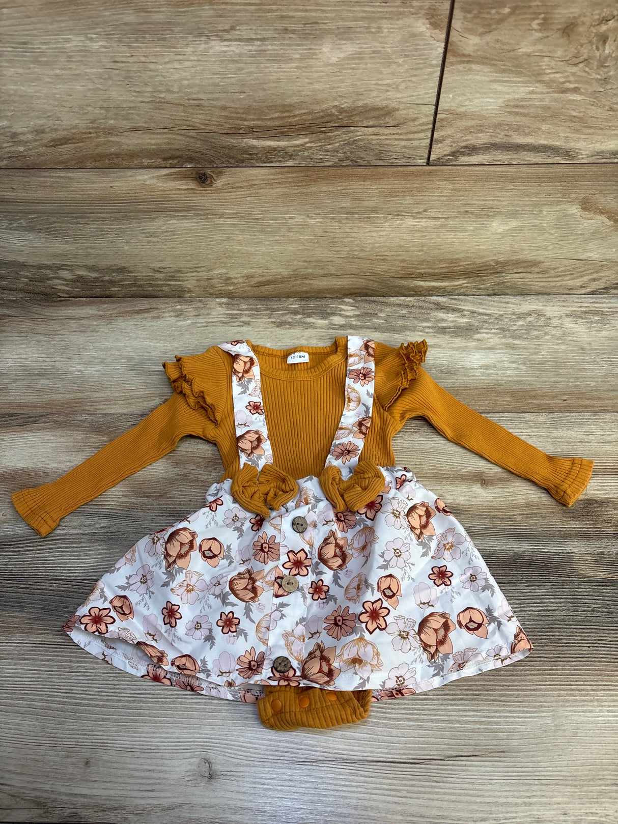 Infant mustard ribbed long sleeve bodysuit with floral suspender skirt on wood background