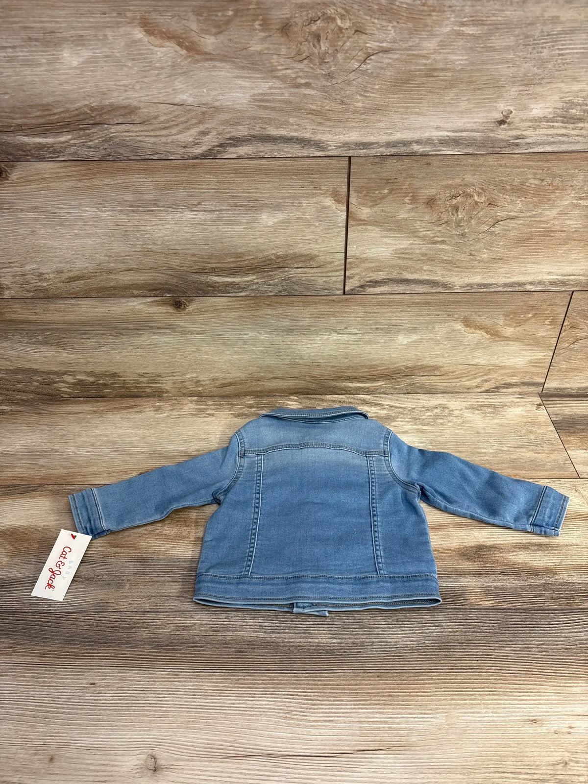 Back view of a light blue toddler denim jacket with label on wooden floor background