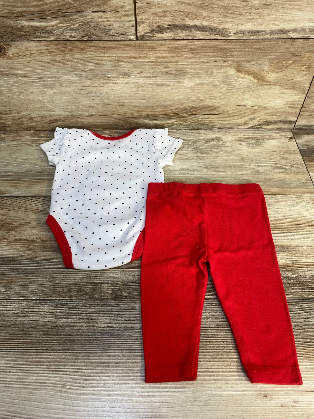 Baby girl outfit with white polka dot bodysuit and red leggings on wood floor