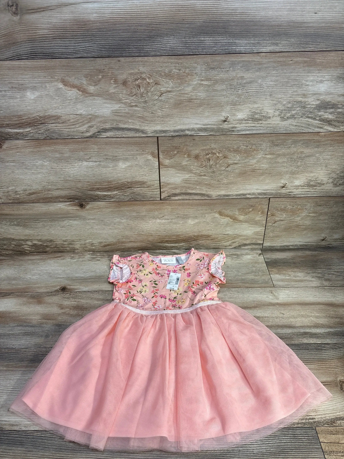 Top-down view of pink Children’s Place girls’ floral knit-to-woven dress showcasing tulle skirt and flutter sleeves on wood background
