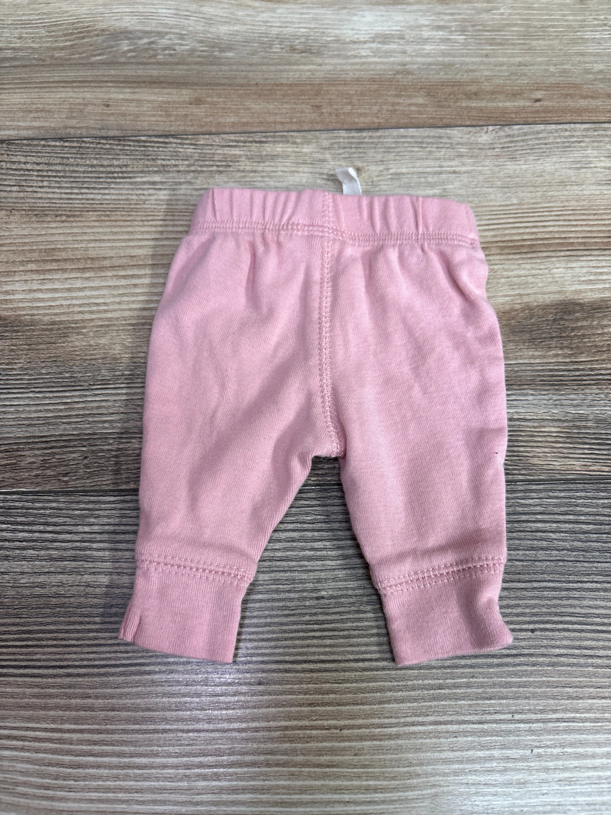 Pink Carter's preemie pants laid flat on a grey wood grain background.