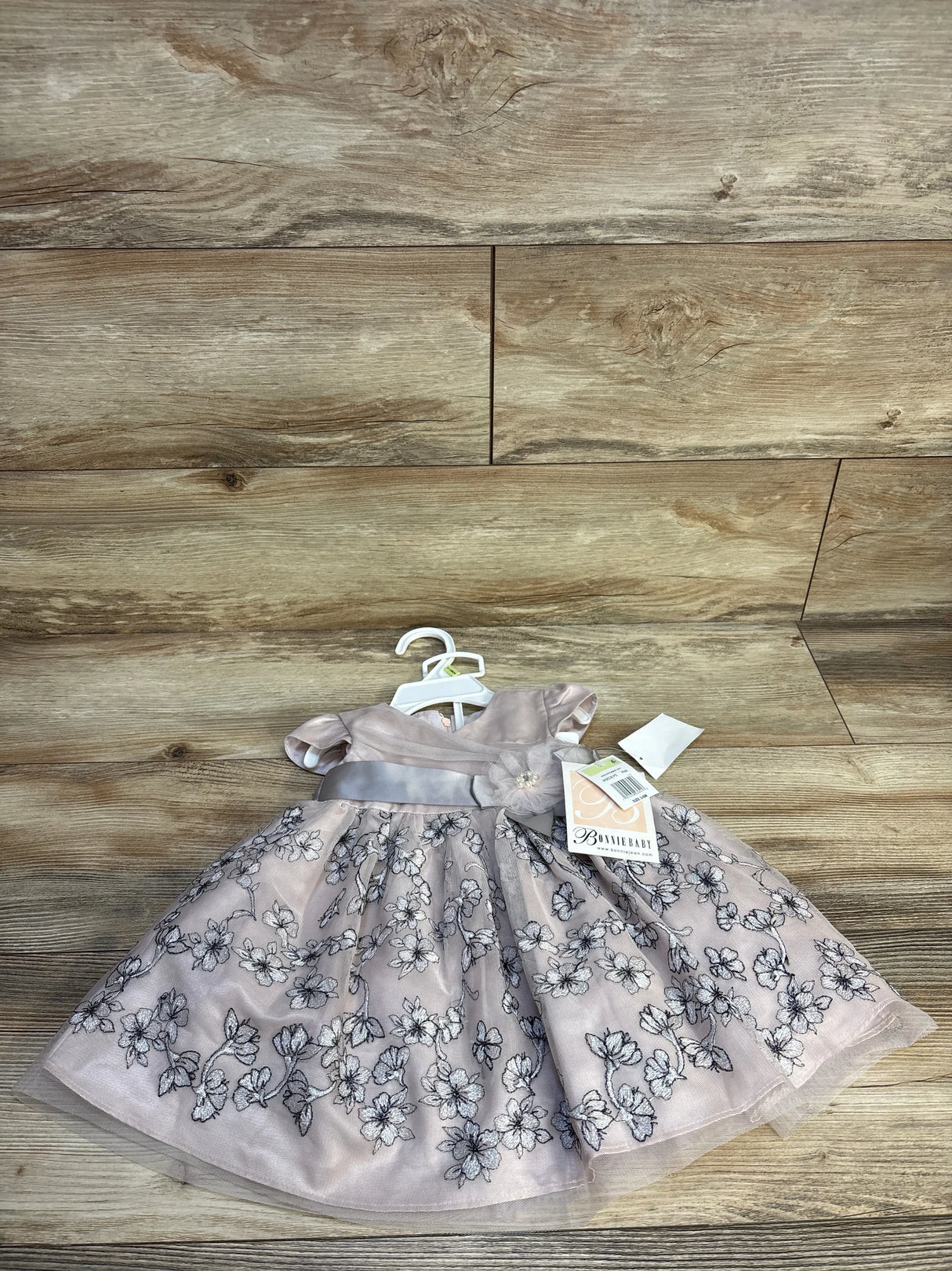 Pink floral embroidered baby dress with short sleeves and satin waistband on wood background