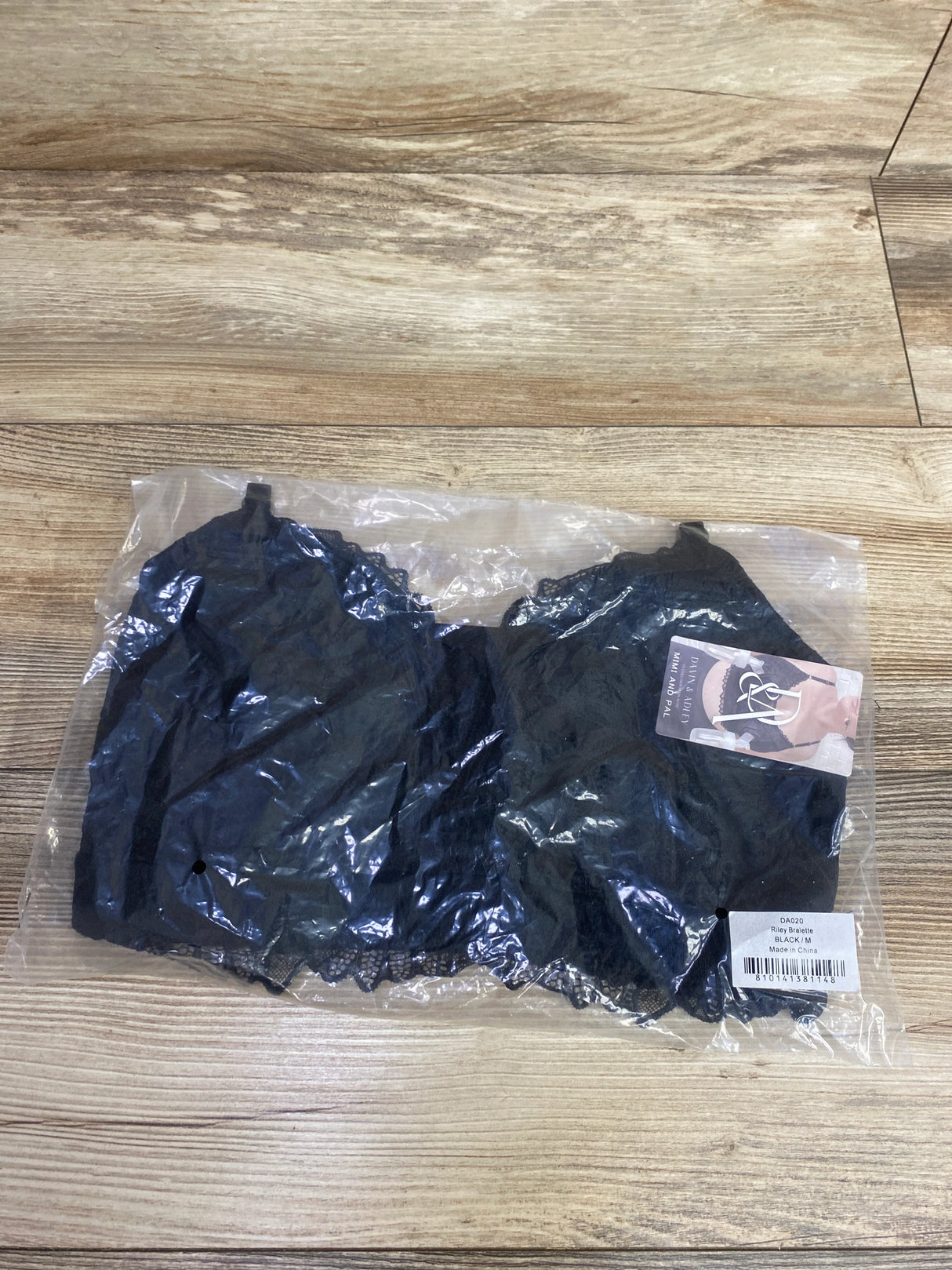 Black lace Riley bralette in medium size packaged in clear plastic on wooden floor