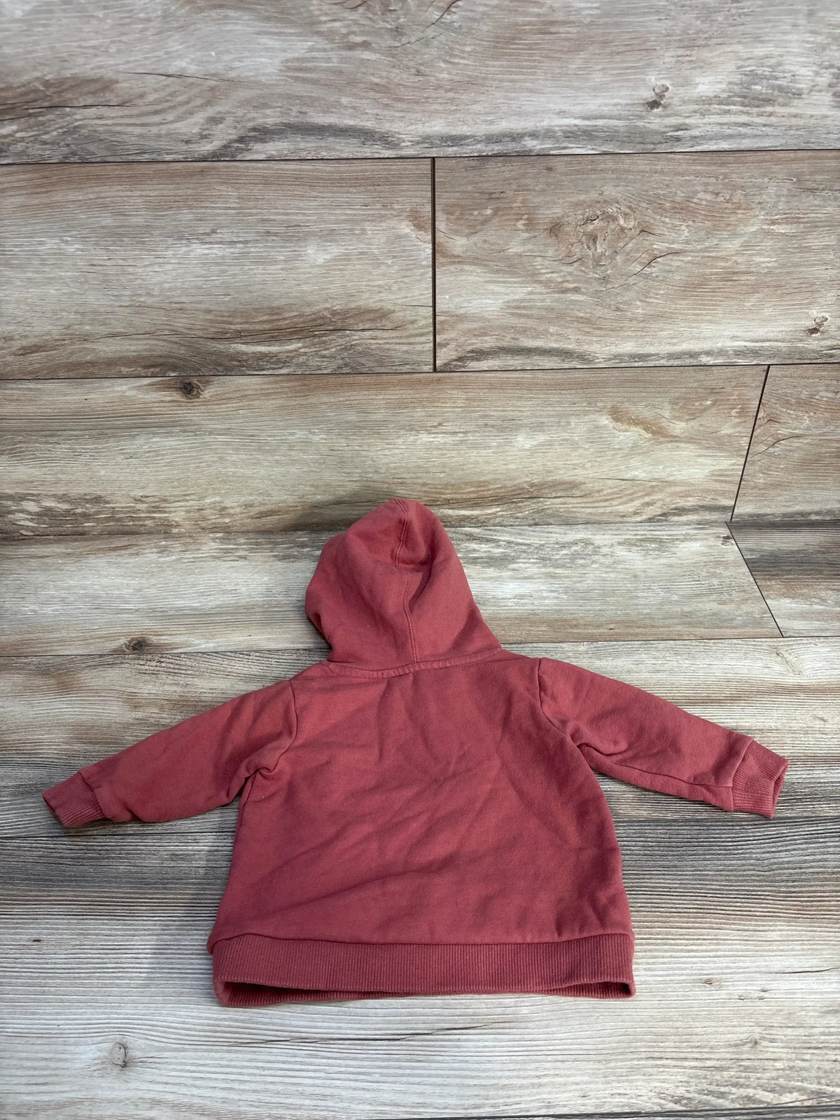 Rust-colored toddler hoodie laid flat on wood floor, back view