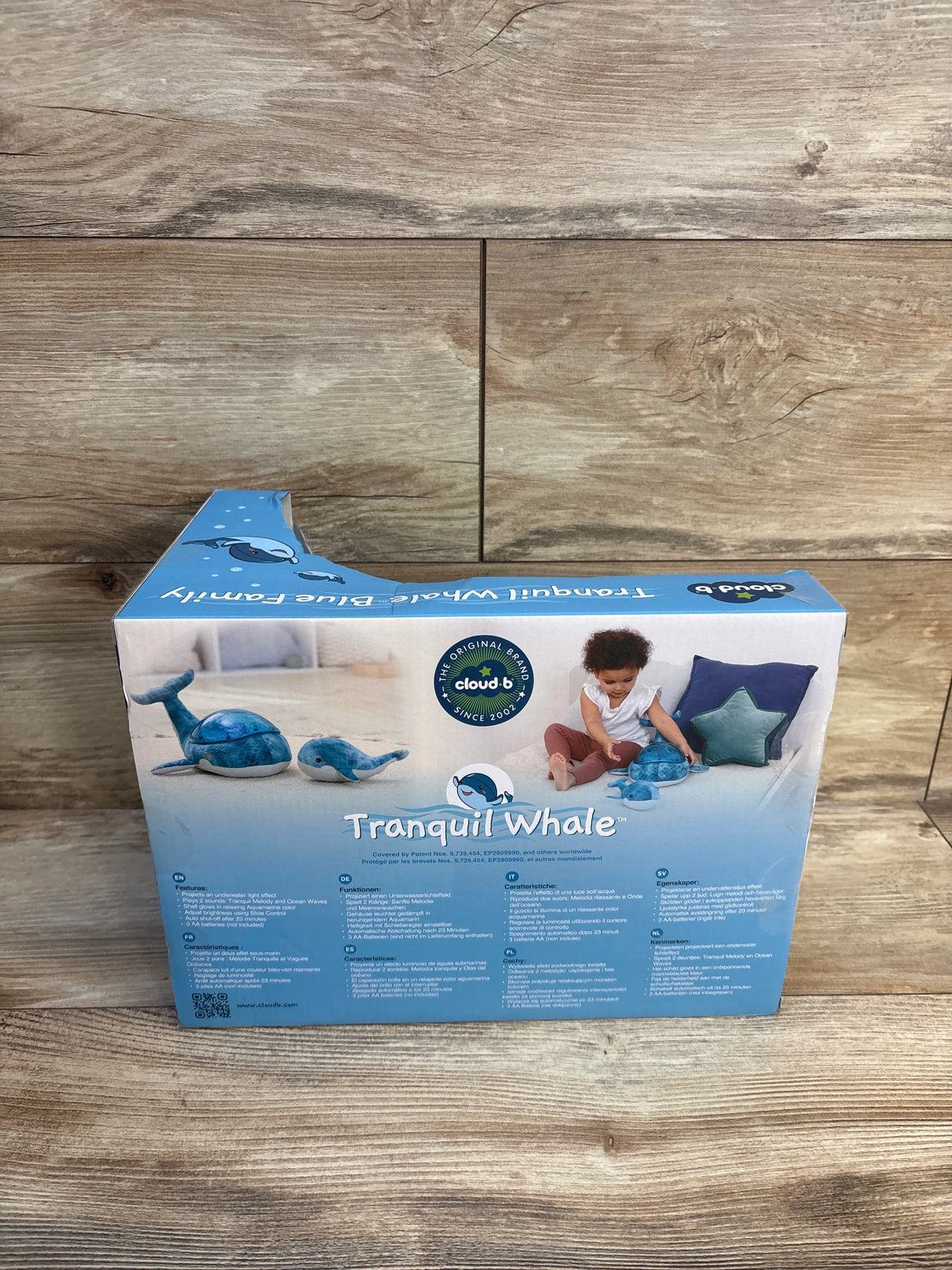 Cloud b Tranquil Whale plush night light box on wood floor, kids toy and baby sleep aid