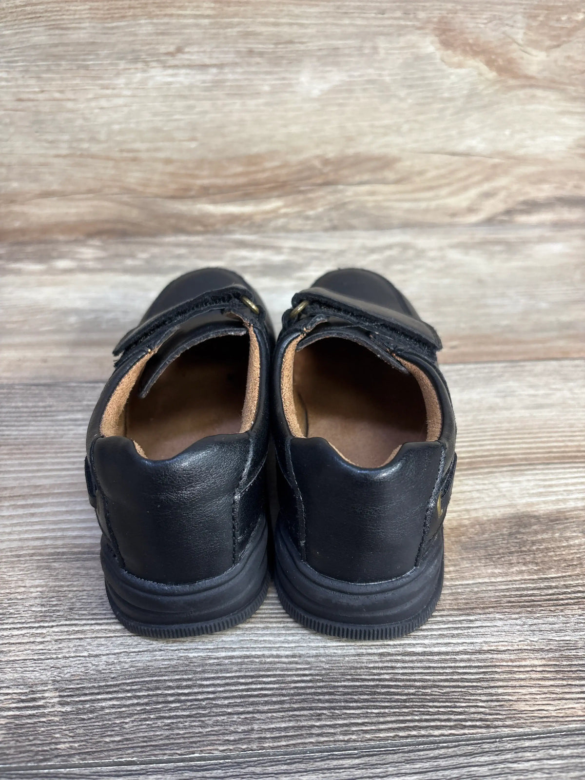 Back view of black Children's Place faux leather dress shoes for kids on a wood surface