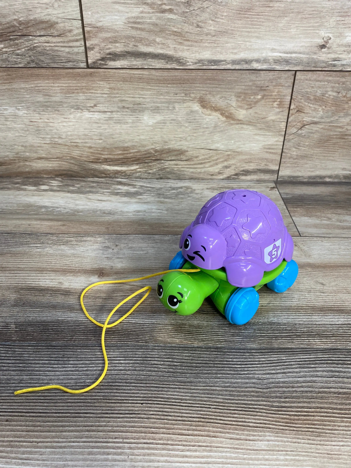 Angled view of LeapFrog Nest & Count Turtle Tower with purple shell, green base, blue wheels and yellow pull string