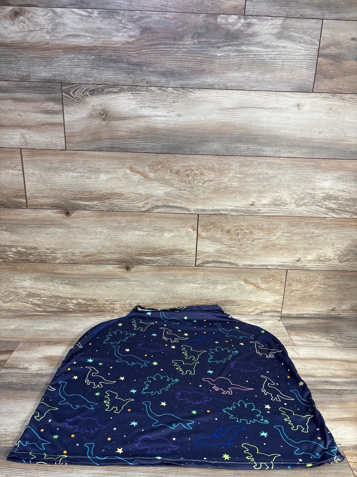 Flat lay of dinosaur print multi-use nursing and car seat cover showcasing navy fabric with colorful dinosaurs on a wood-look floor