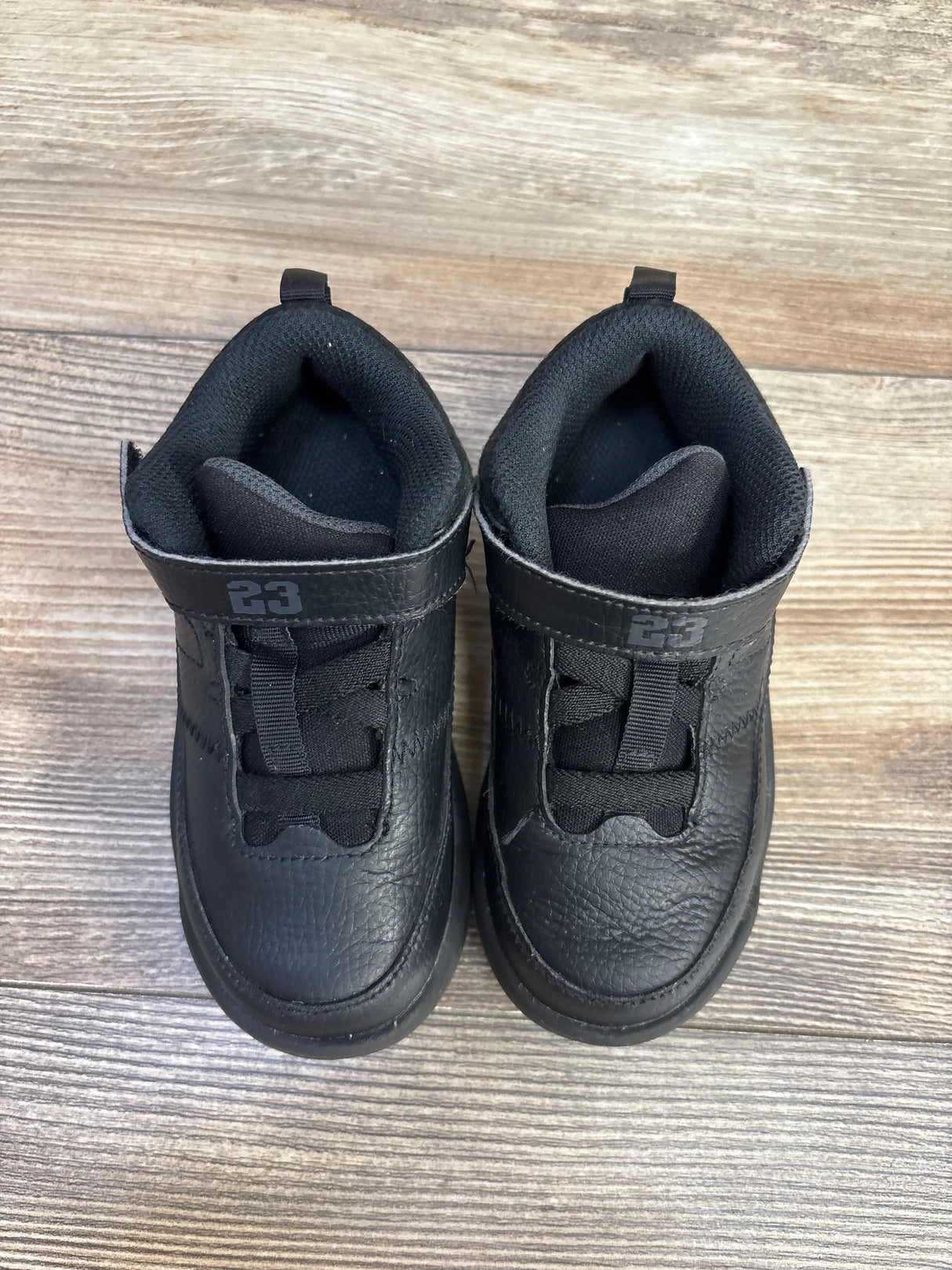 Pair of black toddler sneakers with straps and number 23 on wooden floor