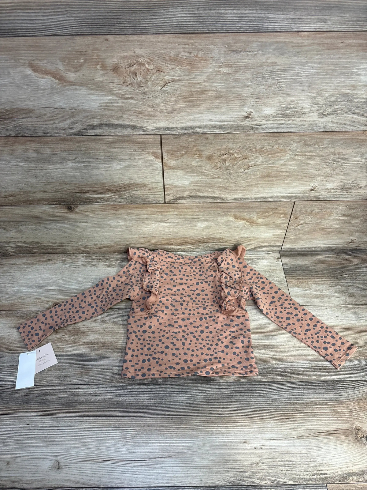 Top view of toddler brown polka dot long sleeve top size 4T showcasing shoulder ruffles and gray spots on wooden floor