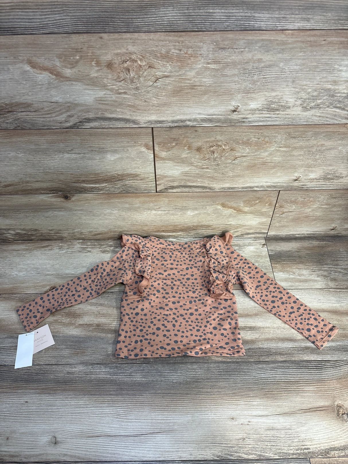 Top view of Grayson Mini ruffled polka dot top, brown 4T, showing long sleeves and shoulder ruffles on wooden floor