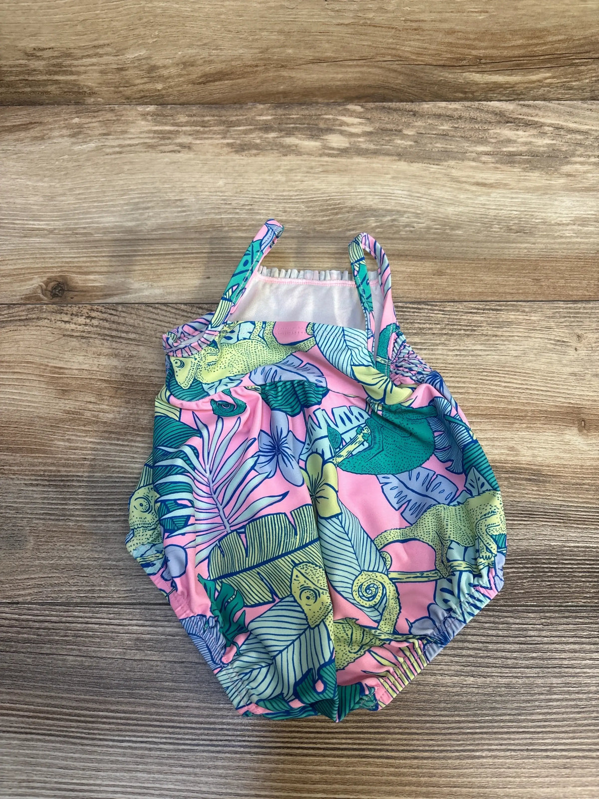 Top-down view of pink Carter’s 1pc baby swimsuit showcasing tropical leaf and chameleon print on wood background