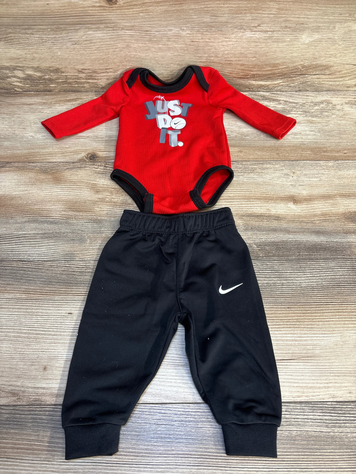 Red Nike baby onesie with 'Just Do It' graphic paired with black jogger pants, ideal for infant sporty outfits.