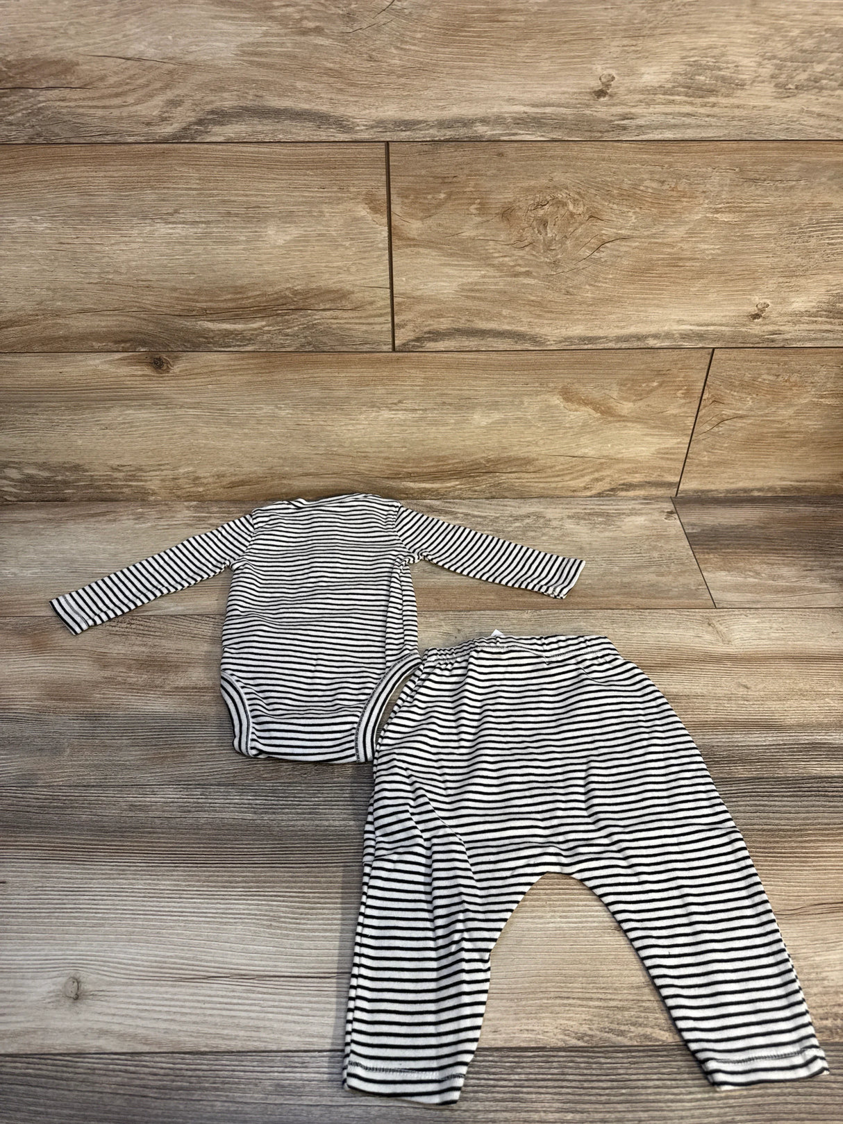 Black and white striped long sleeve baby bodysuit and matching pants on wooden floor