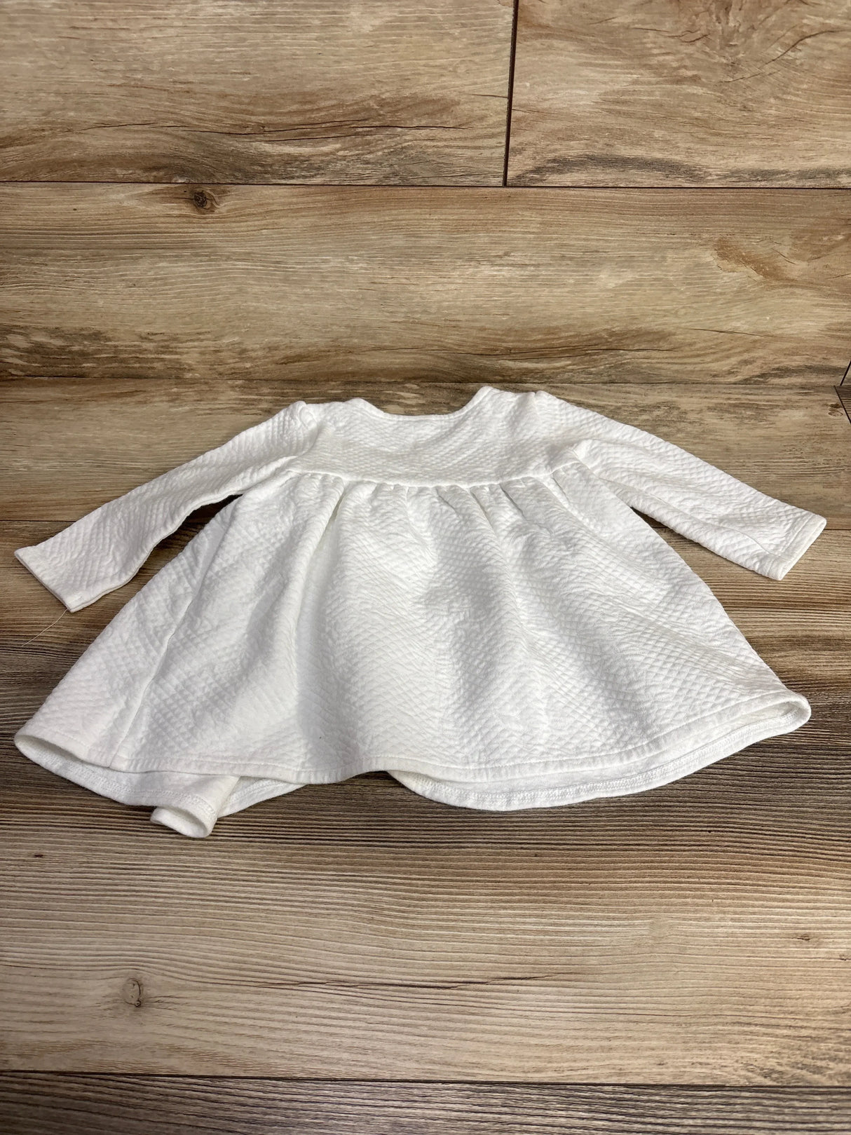 White long sleeve baby dress with textured fabric, laid flat on wood background