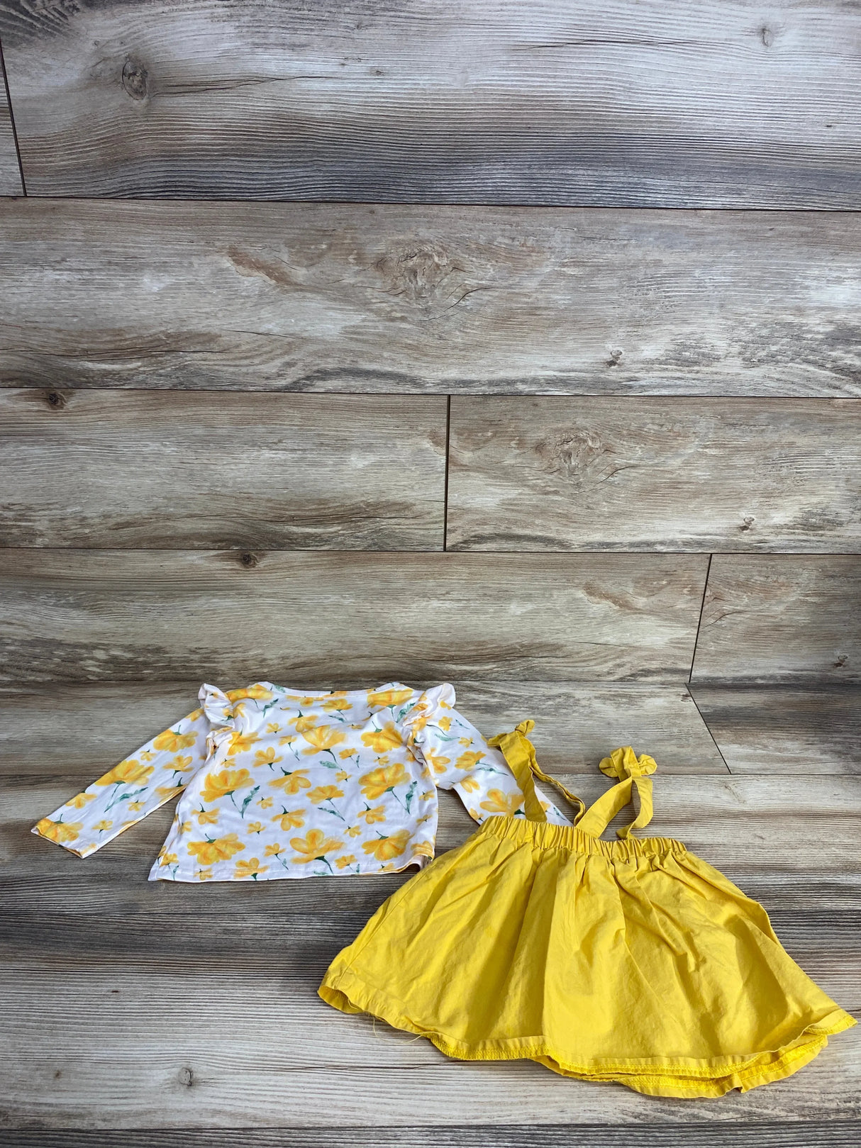 Yellow floral long sleeve toddler shirt and matching yellow suspender skirt on wood background