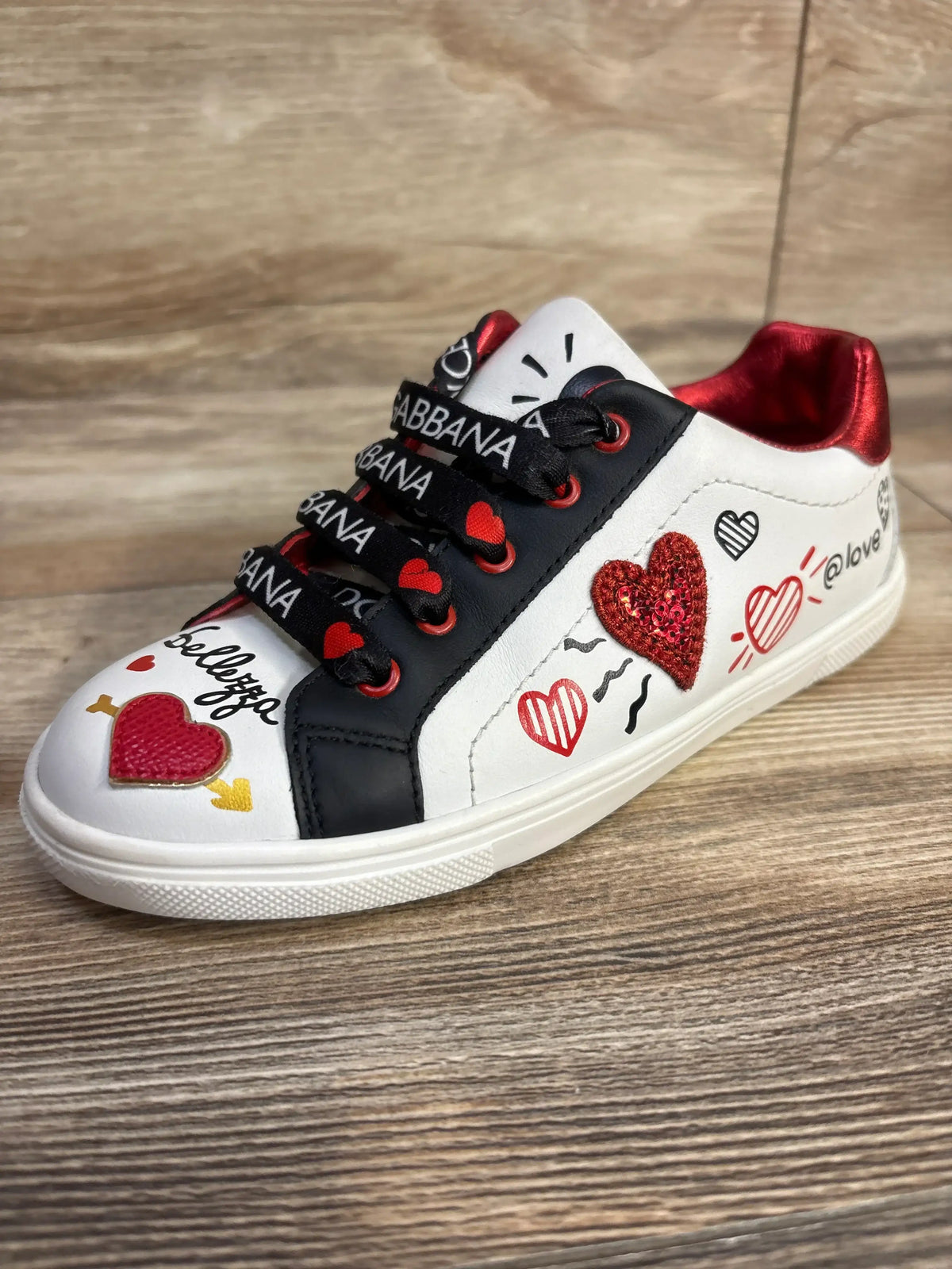 Side view of white Portofino DG Amore calfskin sneaker showcasing heart graphics and black branded laces on a wood surface