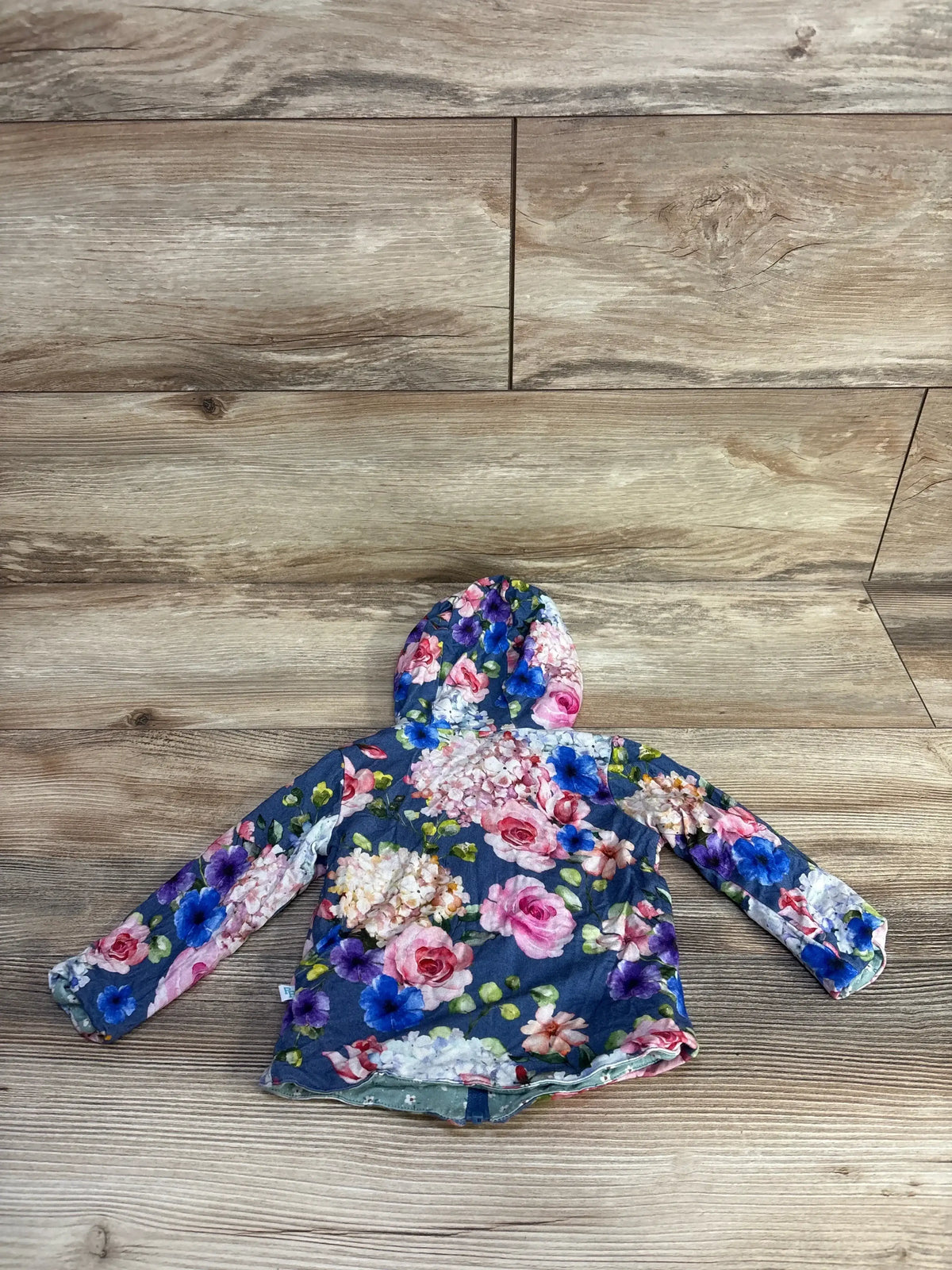 Flat-lay of Posh P reversible baby hoodie (6–12 months) showing blue floral print, hood, and long sleeves on wood floor