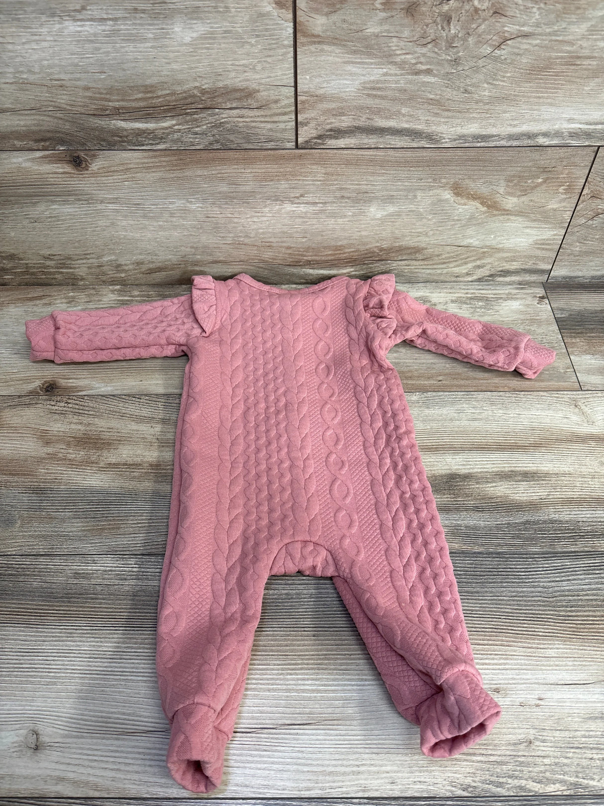 Pink cable knit baby romper with ruffle shoulders on wooden floor