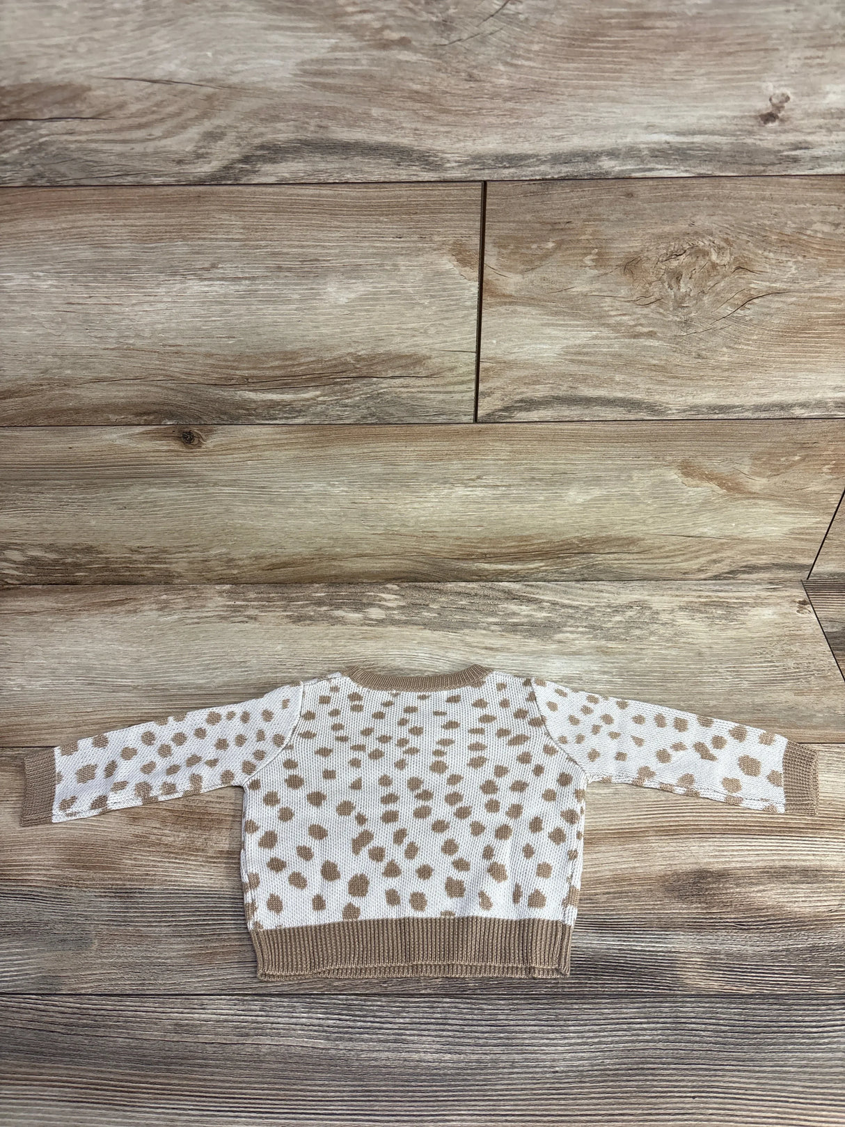 Baby sweater with tan polka dot pattern on wood background, long sleeves, knit design
