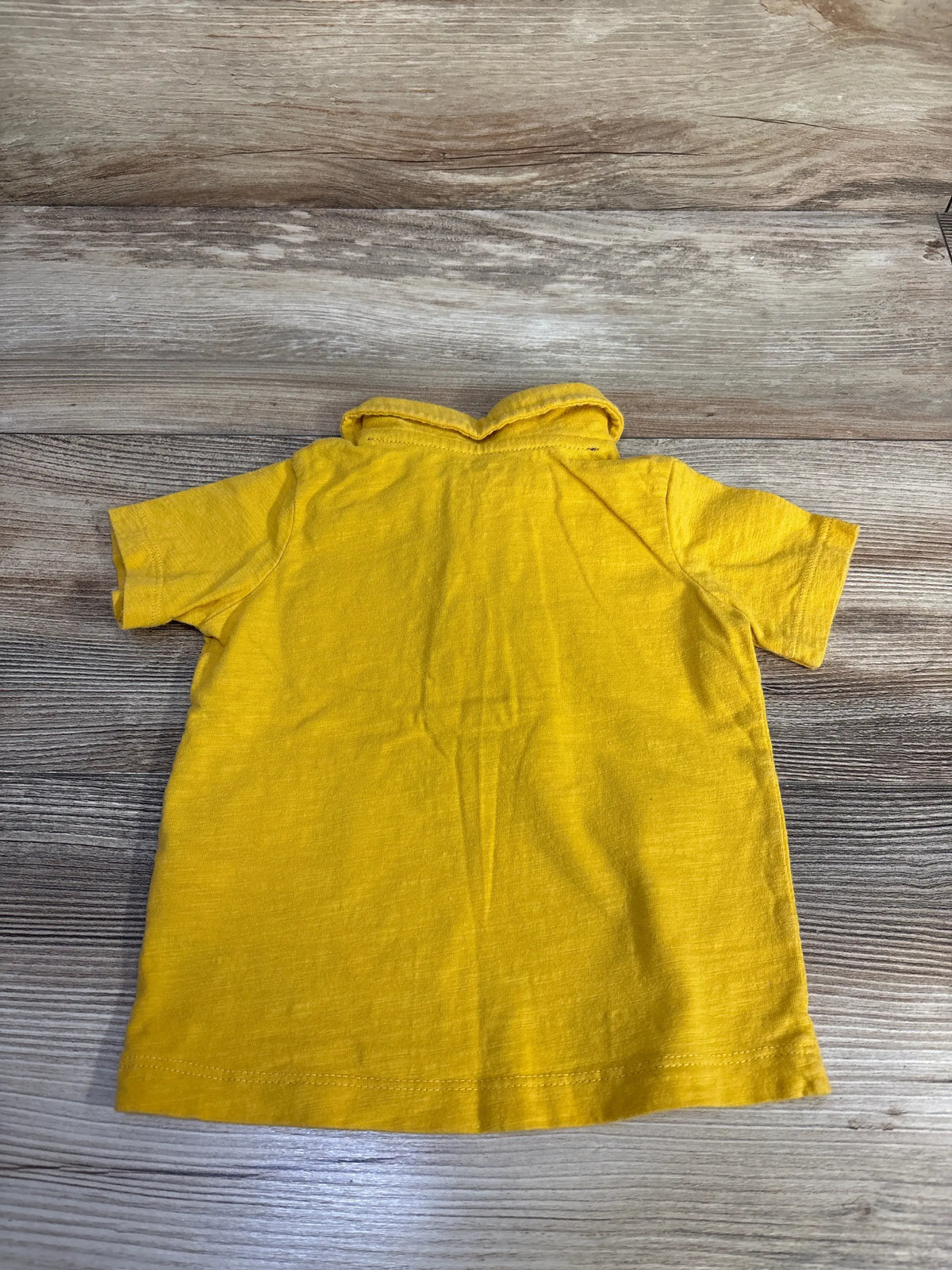 Back view of Carter’s yellow polo shirt showcasing its collar and short sleeves on a wood-grain background